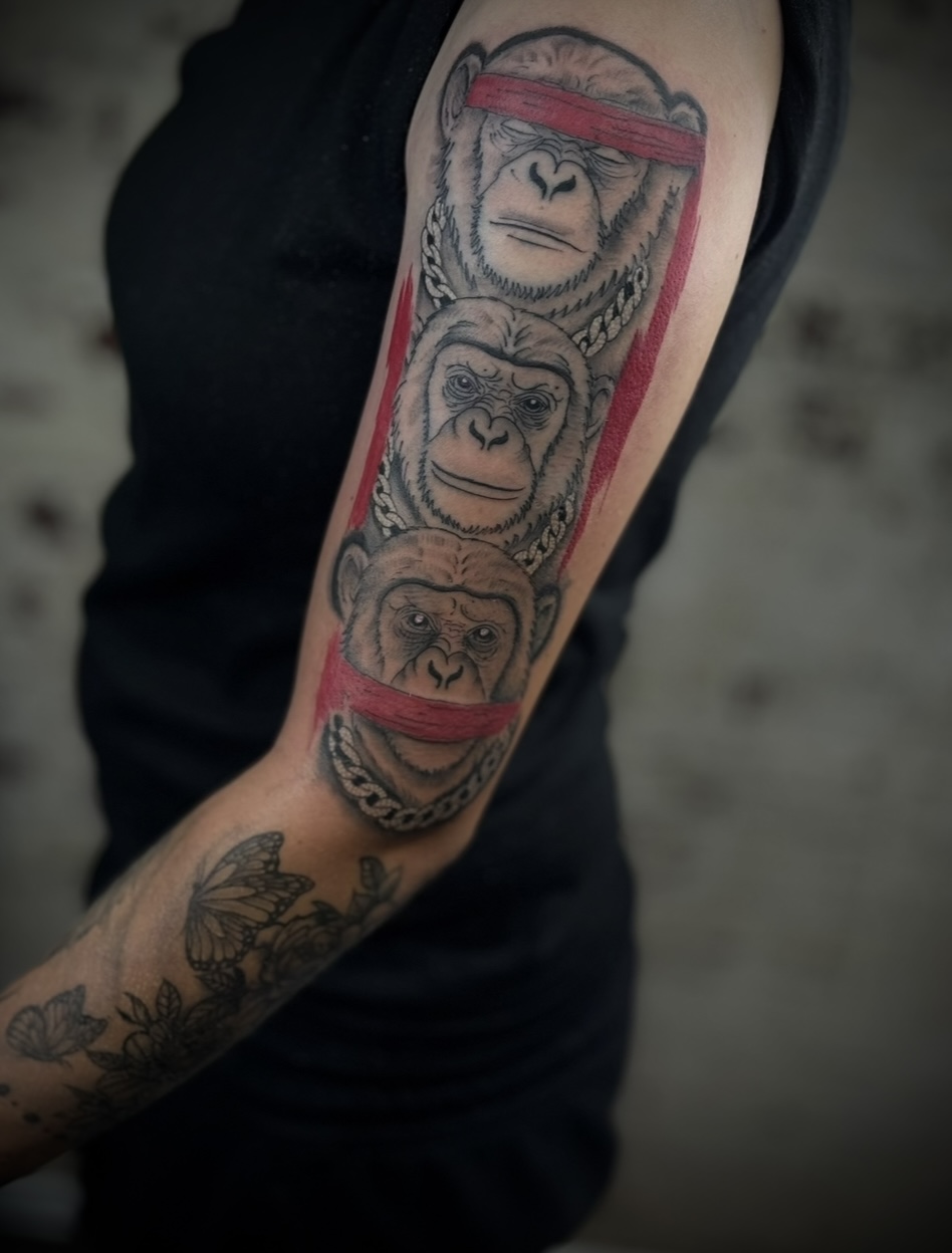Tattoo of three chimpanzee faces stacked vertically on person's arm, with red bands across the eyes of the top and bottom faces.