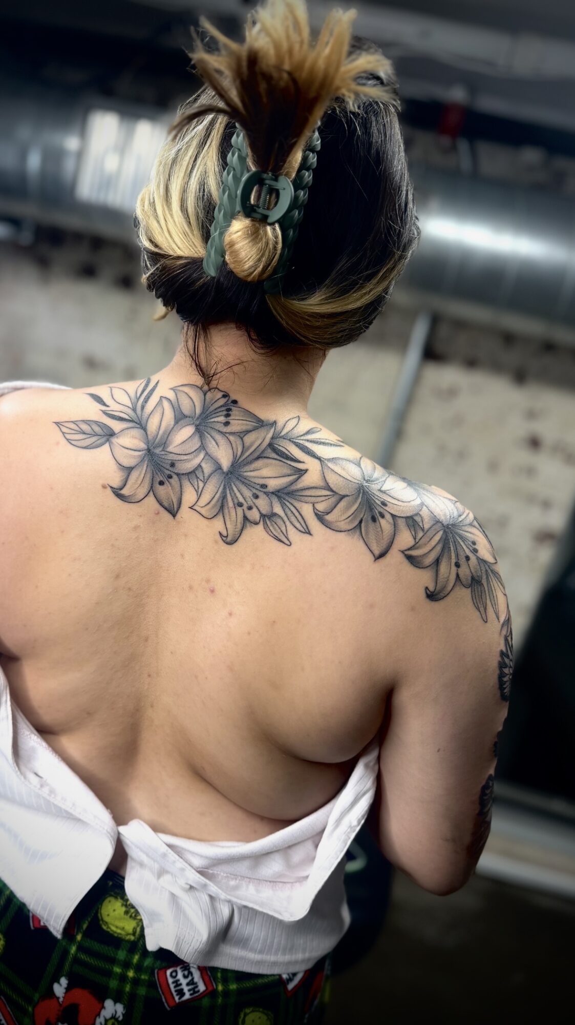 Person with a floral tattoo on shoulder, wearing headphones, with hair in a bun, in an industrial setting.