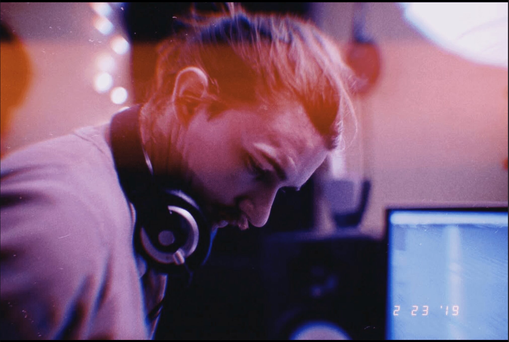 Woman with headphones looking down at a computer screen in a dimly lit room.