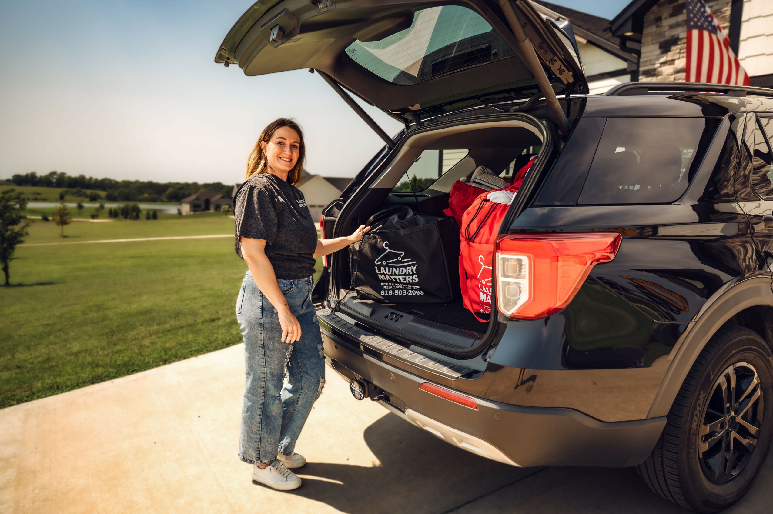 Woman loading a black SUV with a red bag in the trunk outdoors on a sunny day.