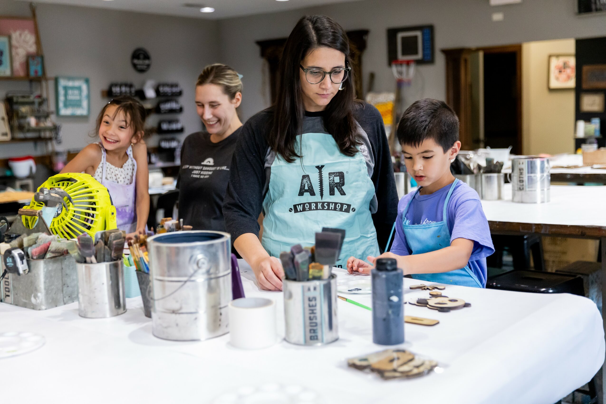Group of children and a woman working on a project at a table in a classroom or workshop setting.