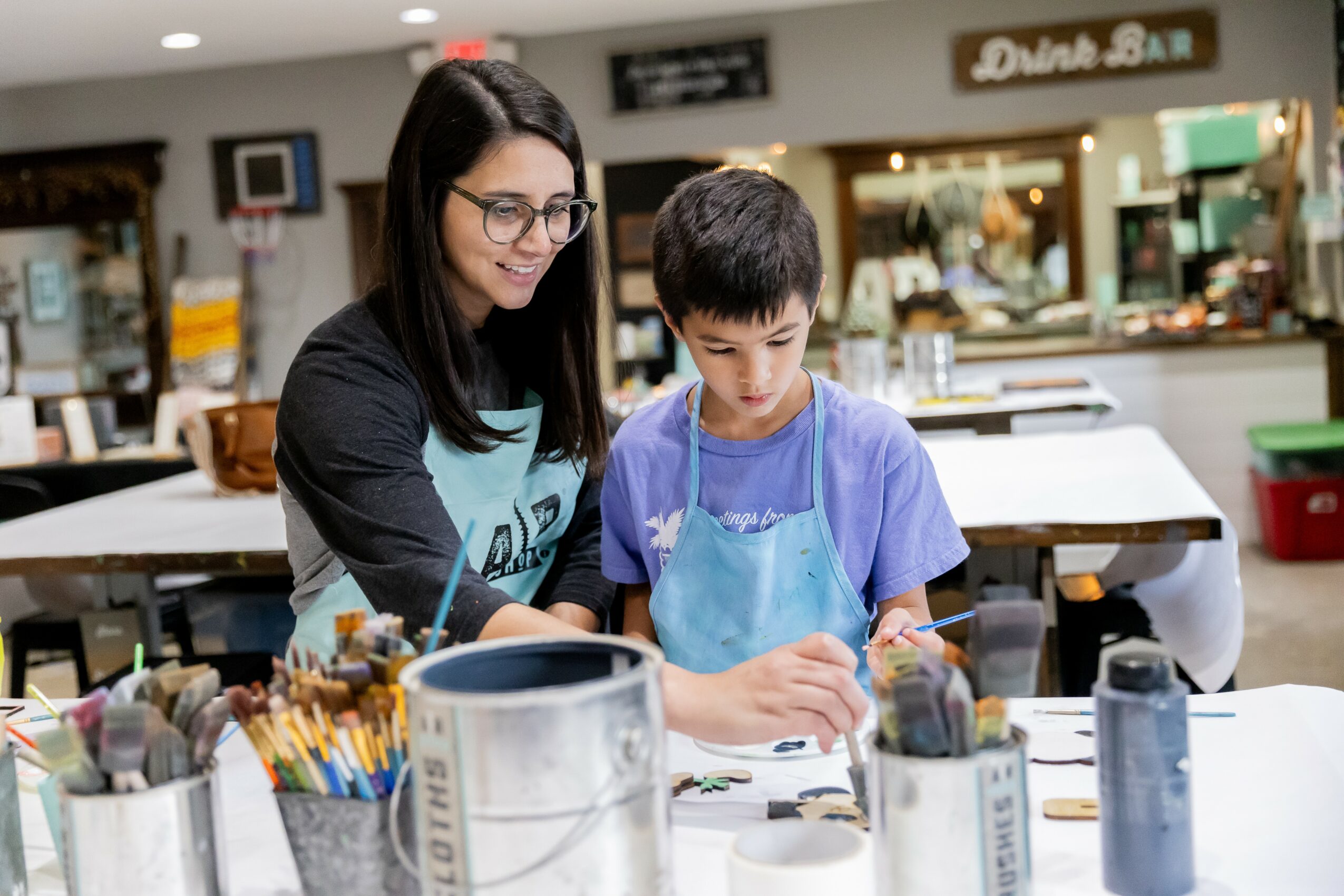 Woman and boy working together at a table in a cafe or restaurant, with various art supplies nearby.