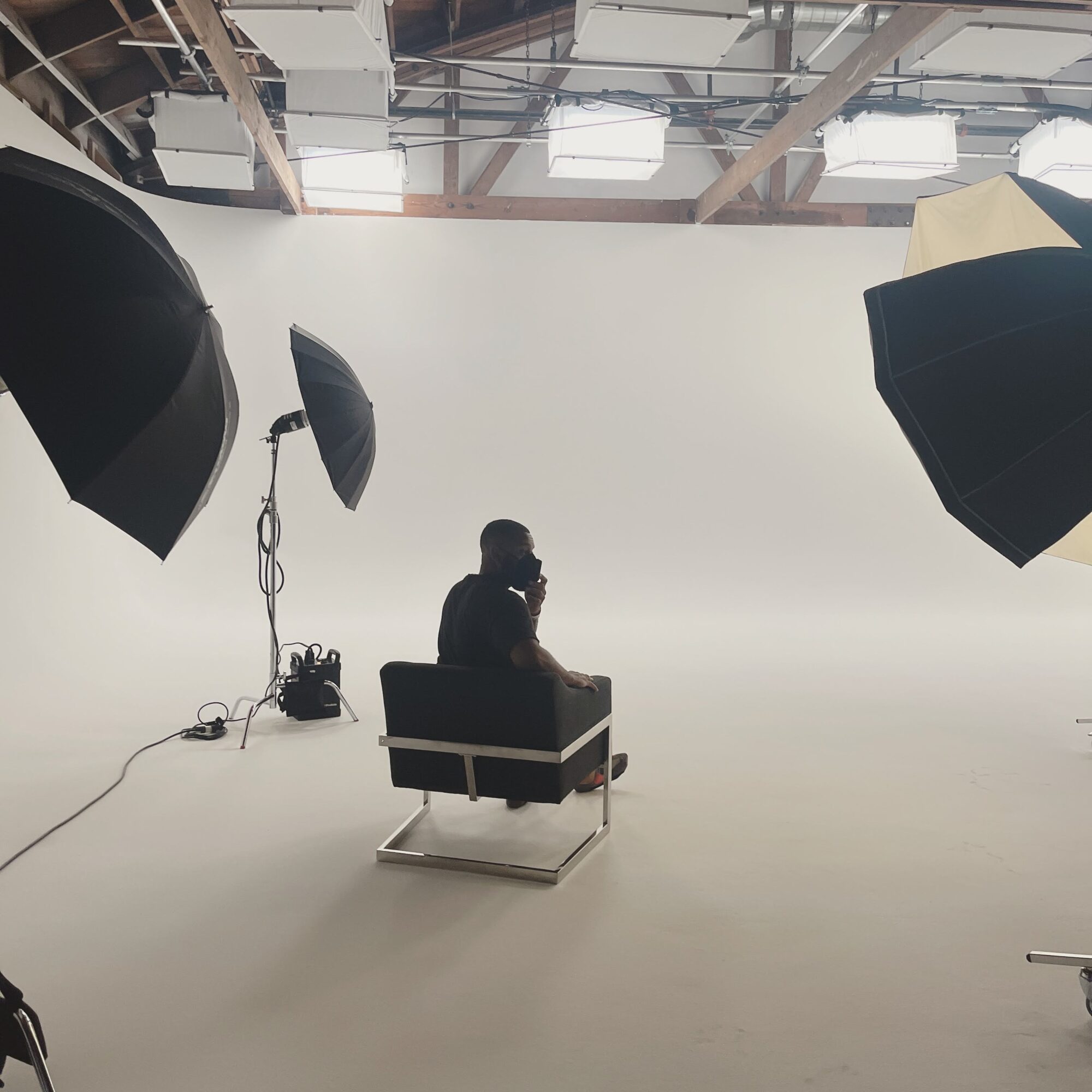 Person sitting on a chair in a photography studio with large studio lights and a white backdrop.