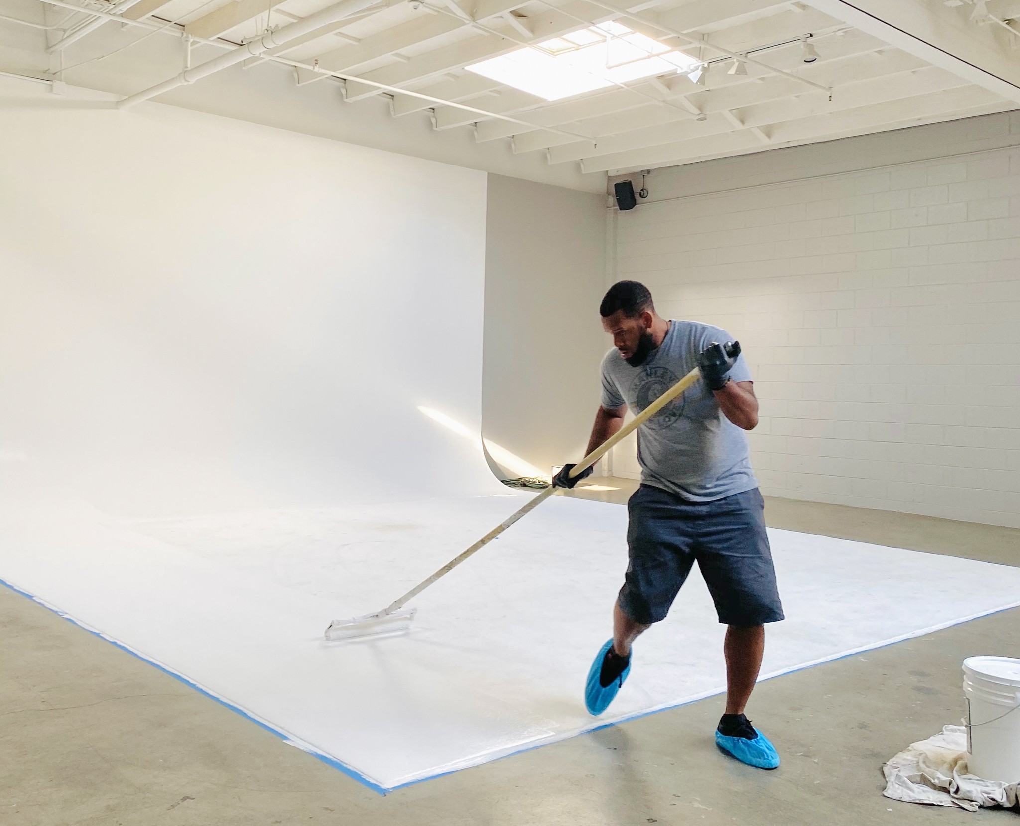 Person sweeping large white floor in a spacious room with white walls and ceiling, using a long-handled broom.