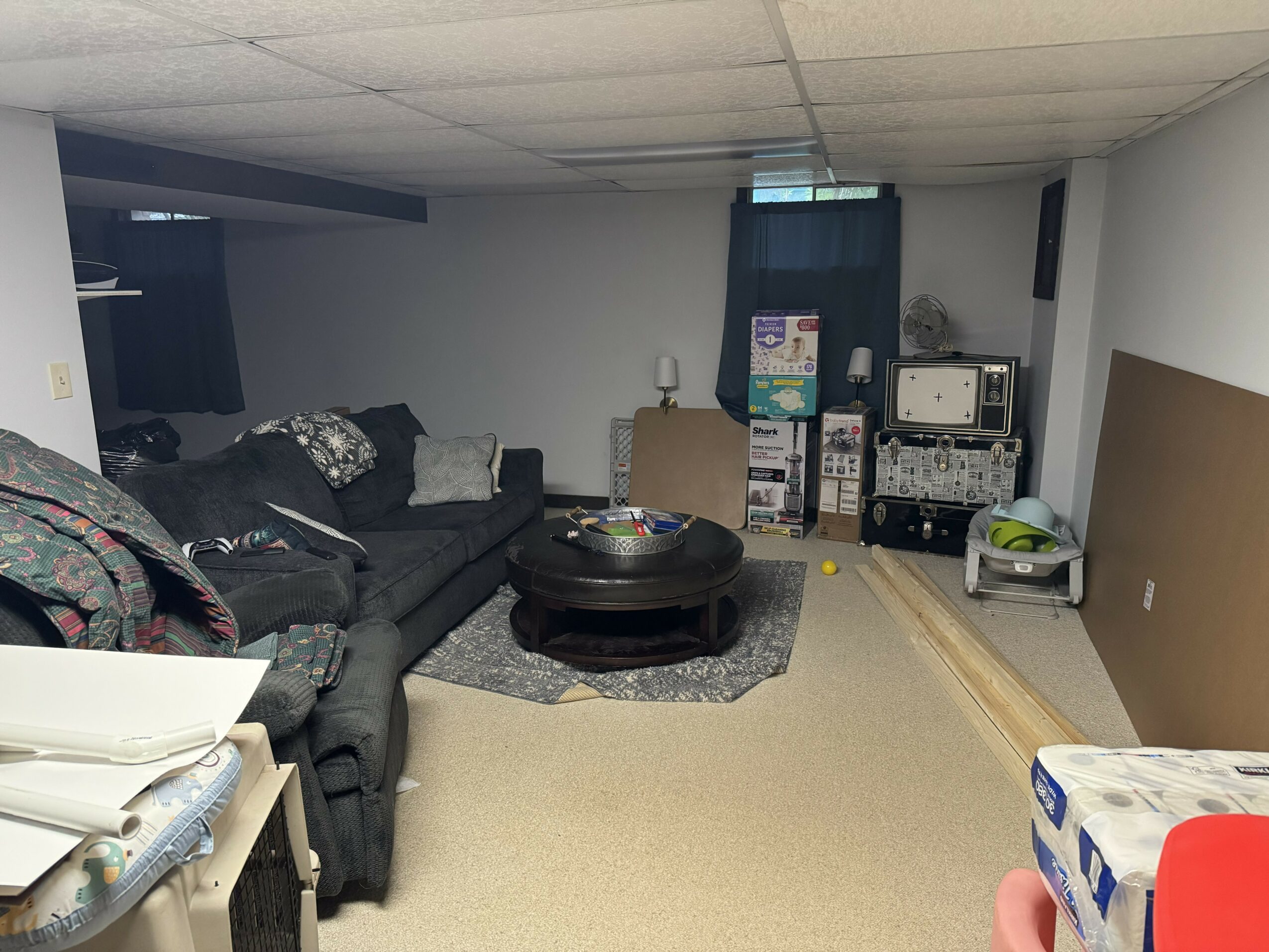 Living room with black sofa, coffee table, and entertainment area, viewed from the right side, with a person holding a box in the foreground.
