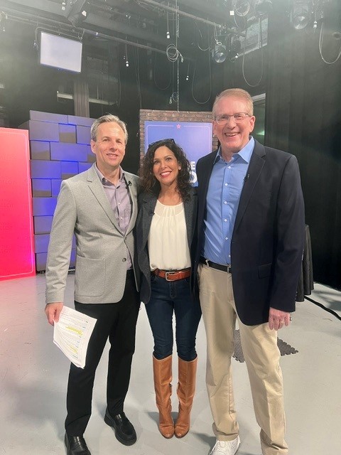 Three people standing together in a studio, smiling, with studio equipment and screens in the background.