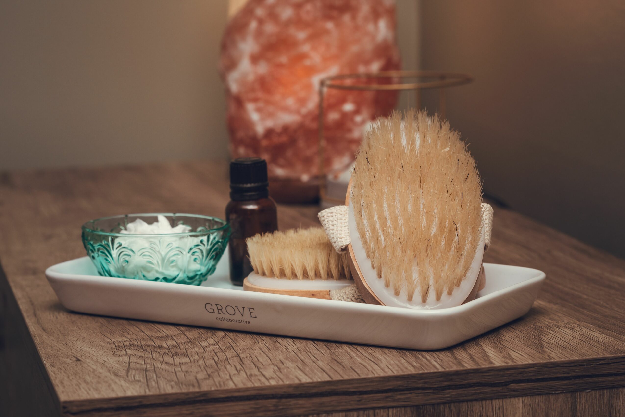 A white tray holds two brushes, a small bottle, and a bowl with white substance on a wooden surface.