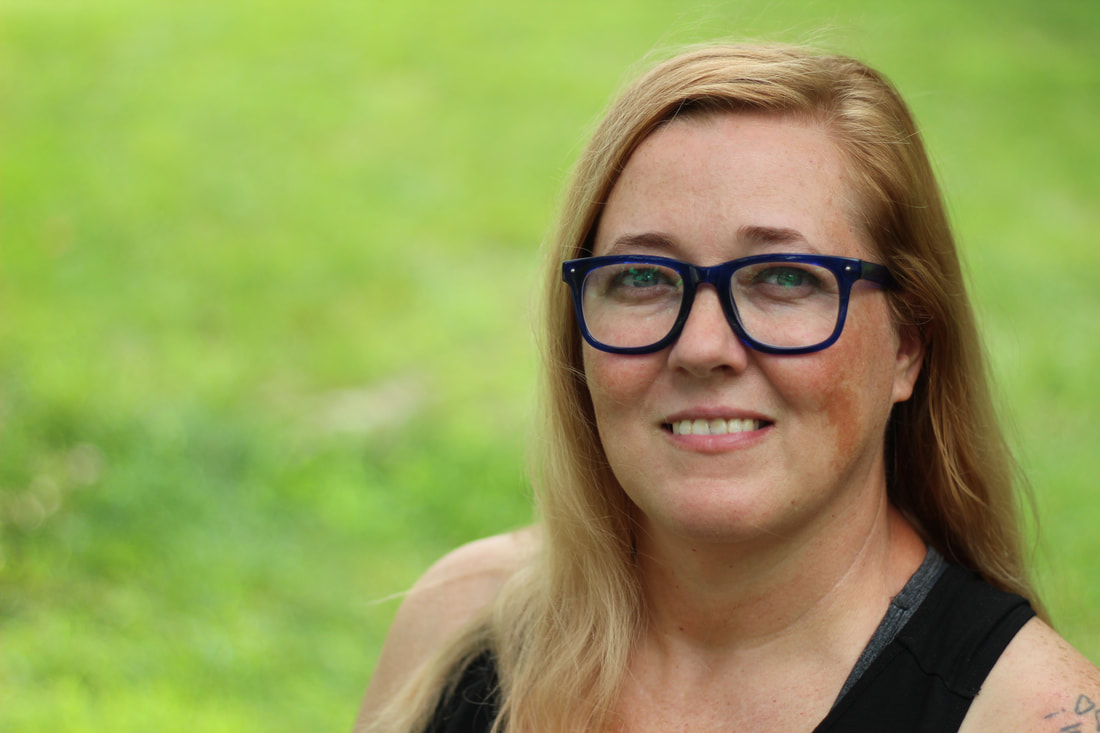 Woman with glasses smiling outdoors with green background