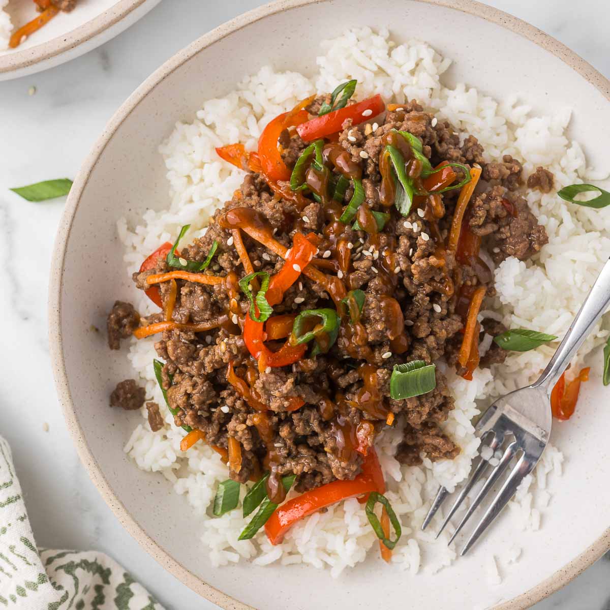 Bowl of cooked ground meat with chopped red and green peppers on white rice, with a fork on the side.