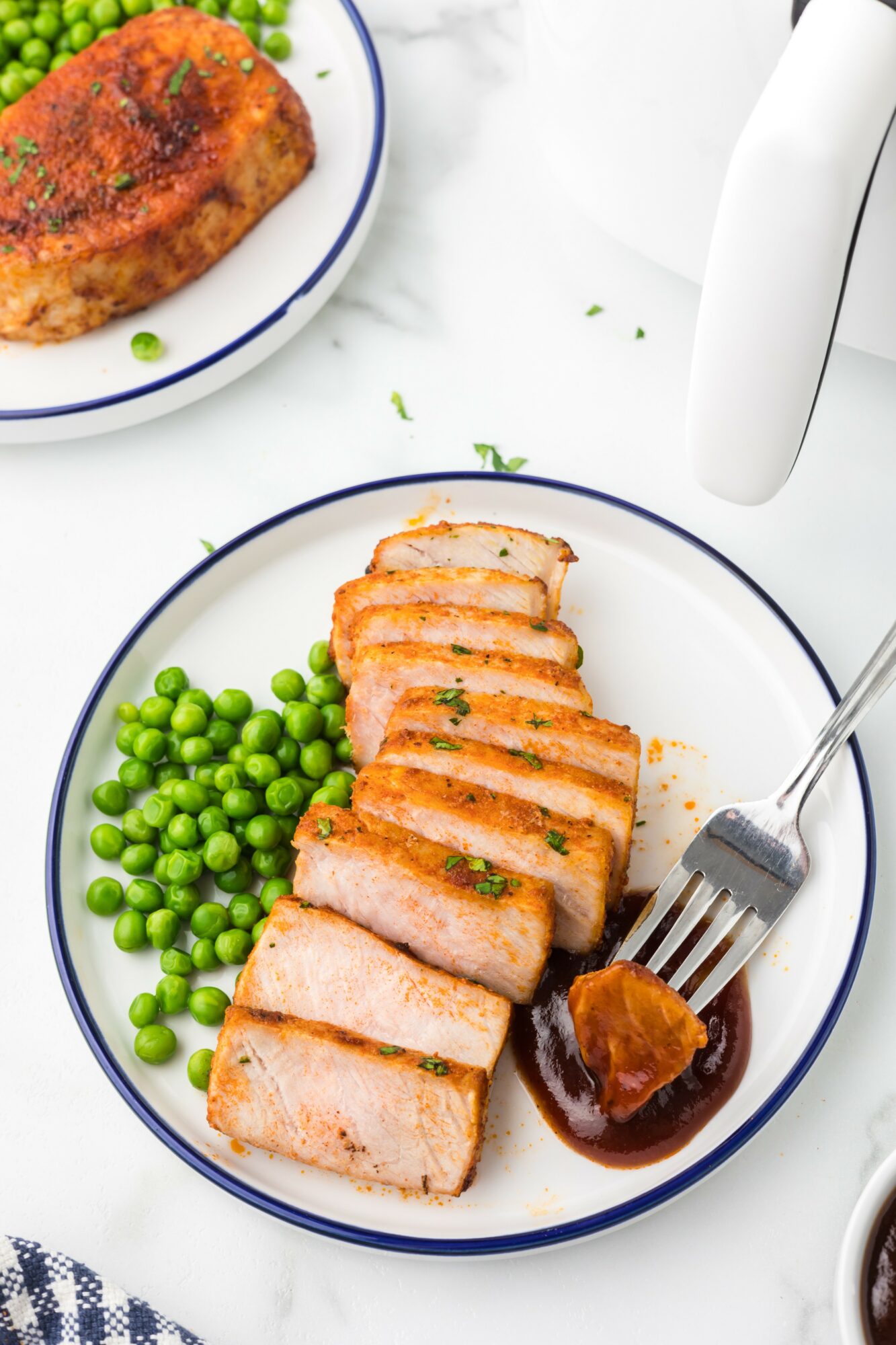 Slices of cooked meat with green peas and sauce on a white plate, with a white background and a fork.