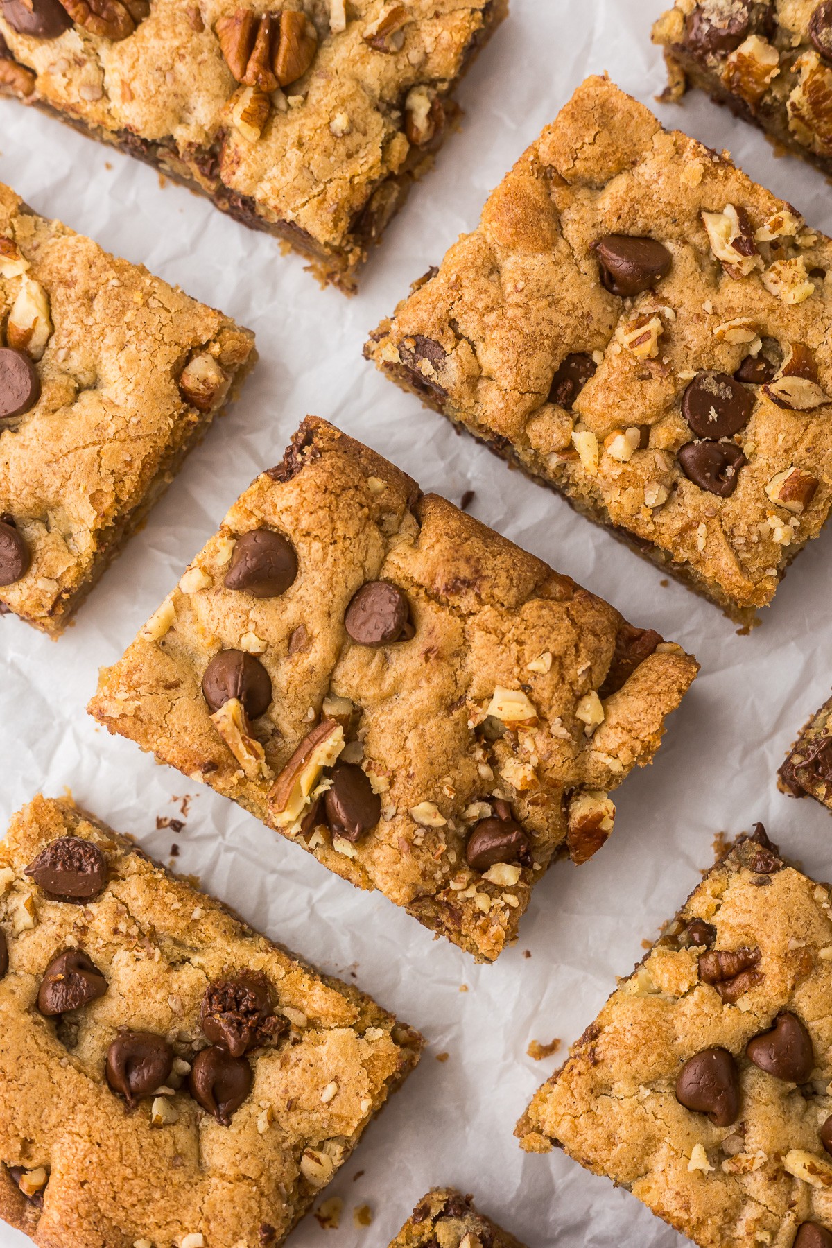 Close-up of chocolate chip cookie bars on parchment paper, showing golden-brown edges and chocolate chips.