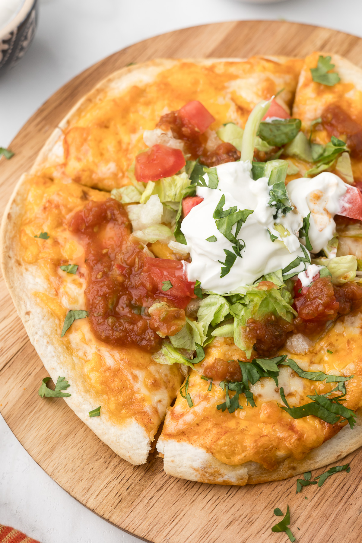 Pizza topped with lettuce, tomatoes, sour cream, and herbs on a wooden board.