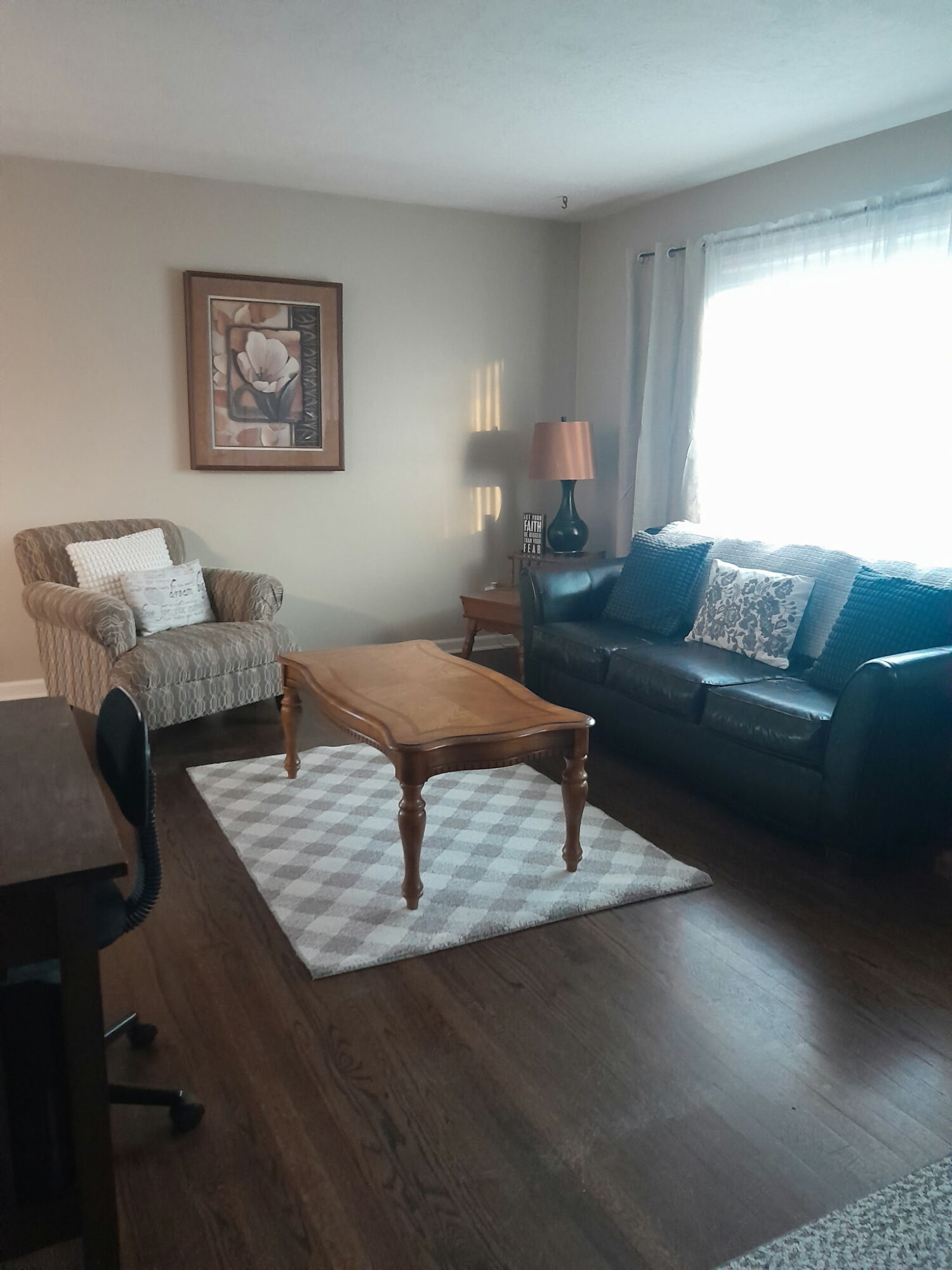 Living room with a striped armchair, a dark sofa, a wooden coffee table, a lamp, and a window with curtains.