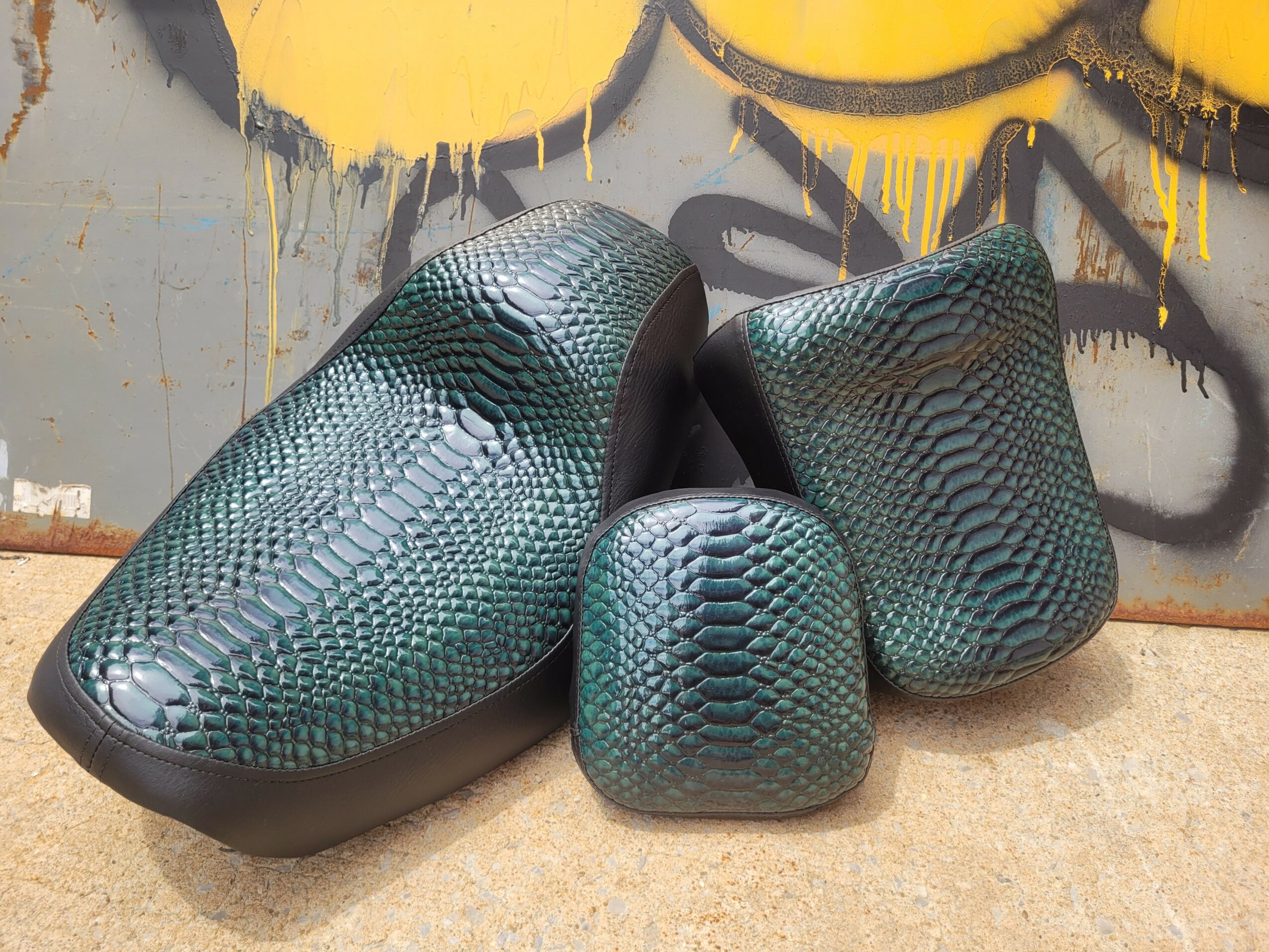 Four shoe-shaped objects with a textured, reptile-like pattern, placed on a surface with graffiti in the background.