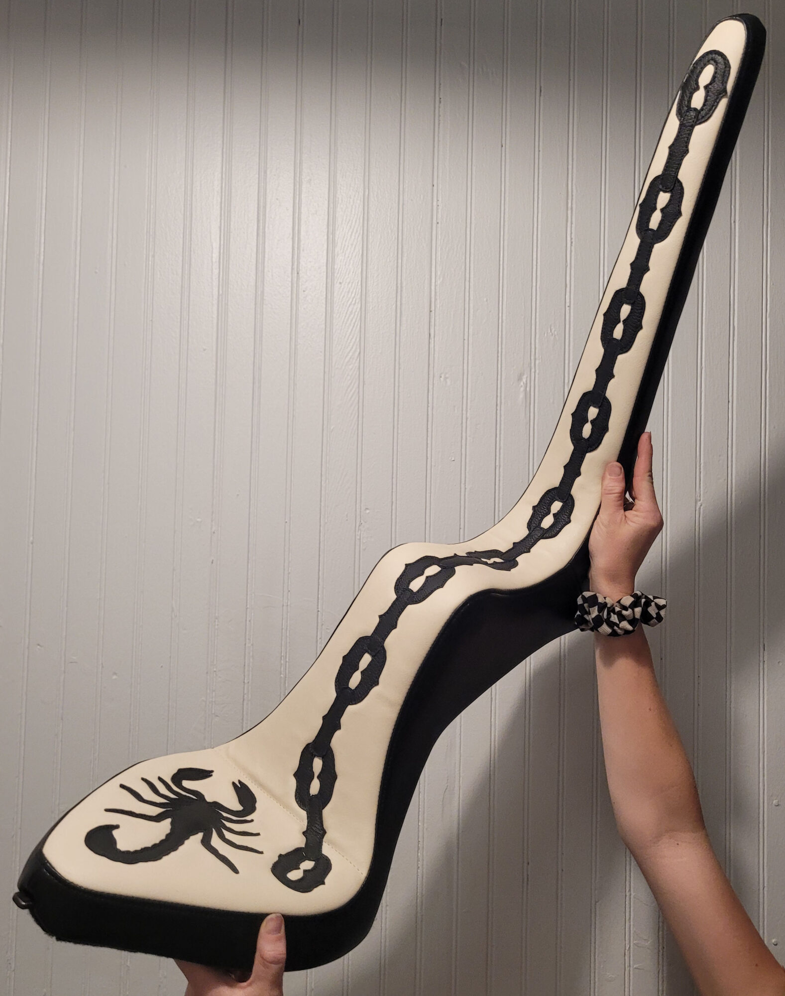 Person holding a large guitar-shaped object with a chain design, against a plain wall.