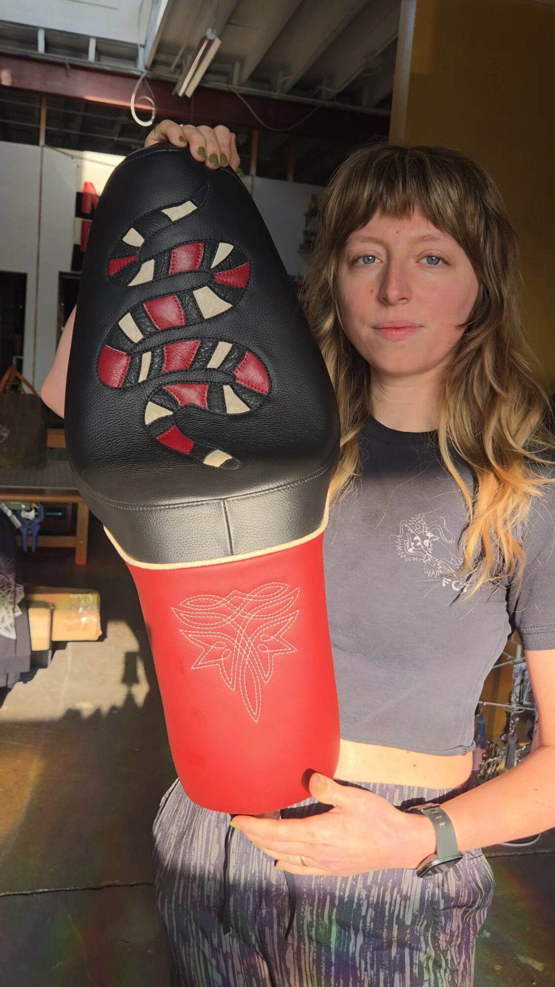 Person holding a shoe with a black upper and red sole, showing the sole's design, in an indoor setting.