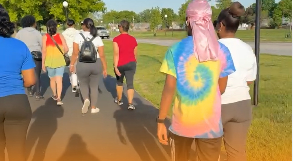 Group of people walking outdoors on a sunny day, some wearing backpacks and colorful clothing.