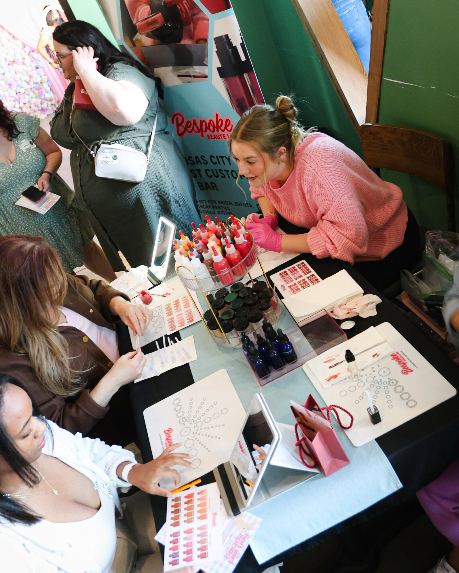 Group of women sitting at a table with makeup, brushes, and beauty products, engaging in a beauty or makeup event.
