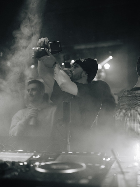Person taking a photo or video with a smartphone at a crowded event with smoke and bright lights.