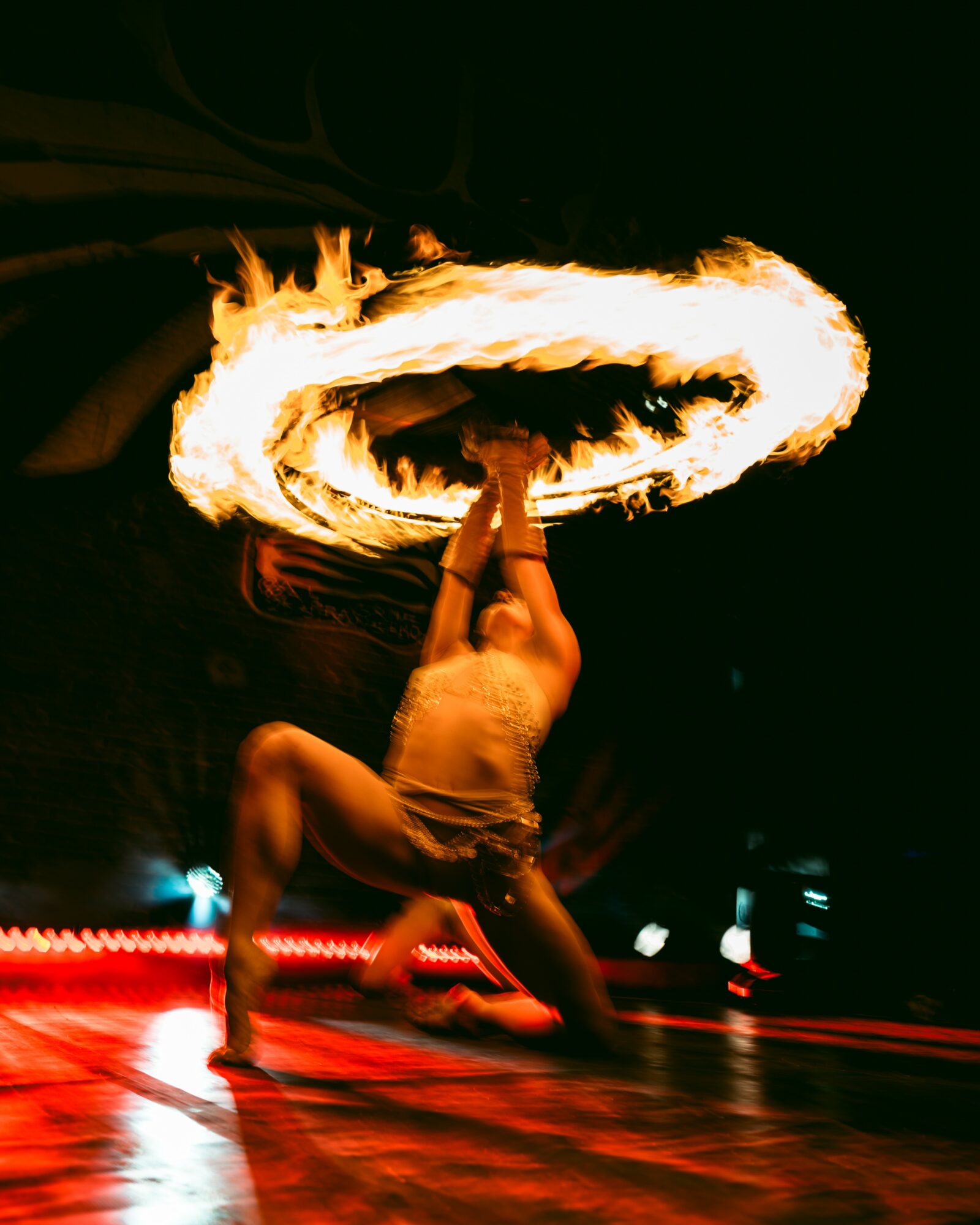 Performer spins fire in a circle above their head at night, with flames creating a ring of fire.