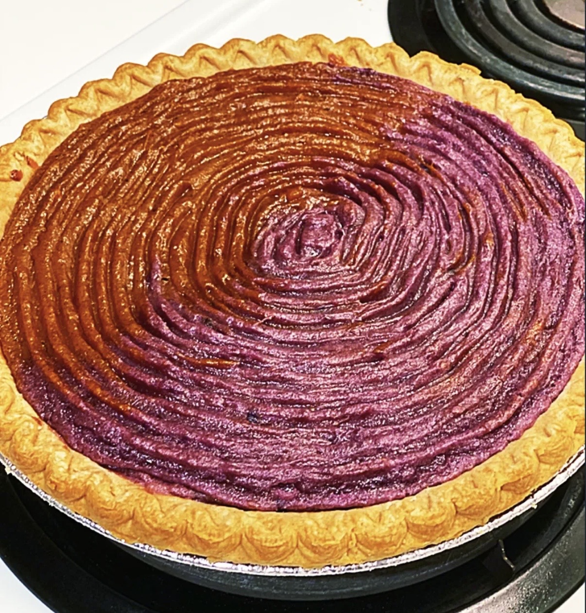 Round tart with a golden crust and a purple swirl pattern on top, on a stovetop. Word count: 20