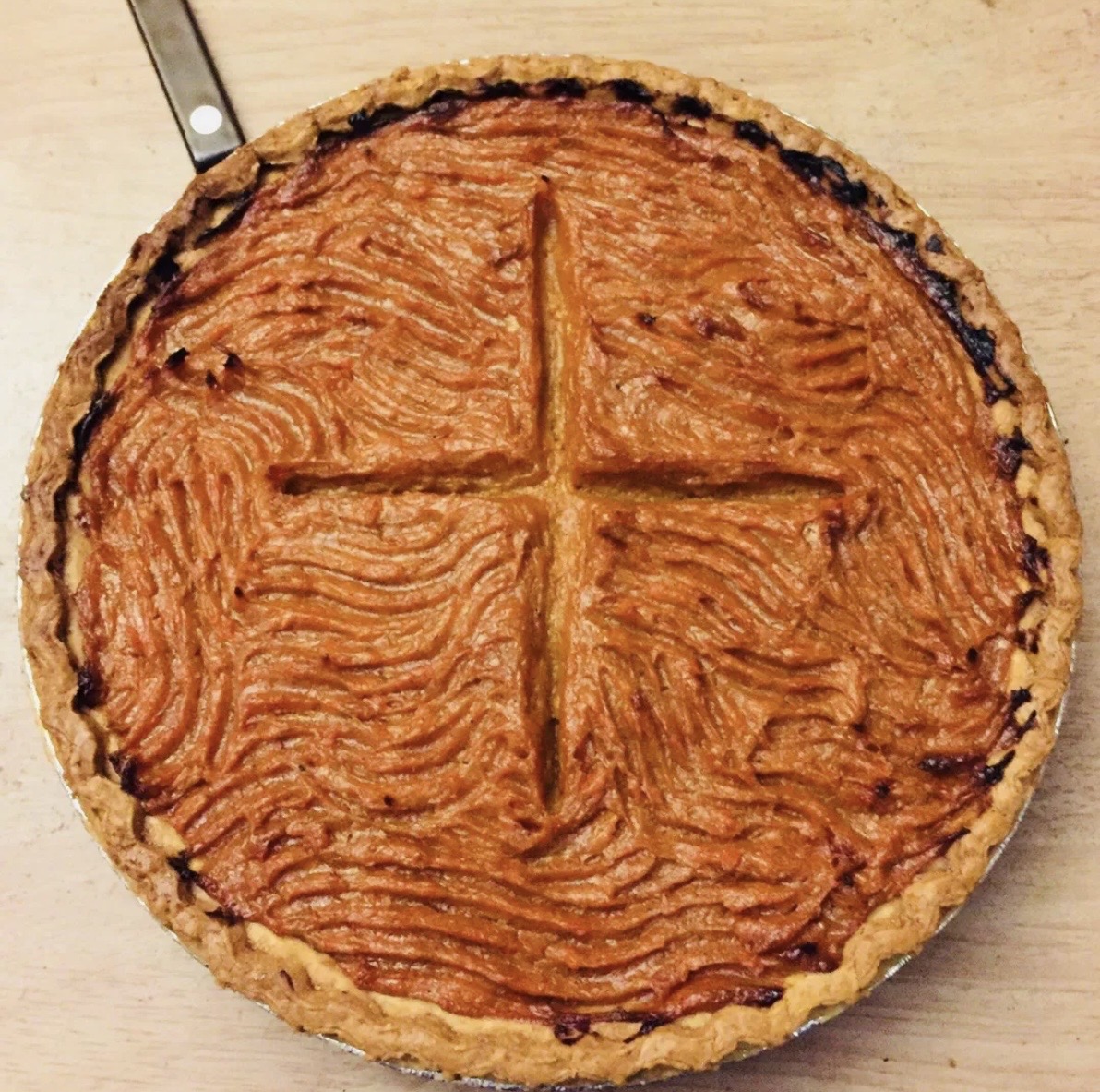 A round pie with a golden crust and a textured, orange filling, divided into four sections with a cross pattern.