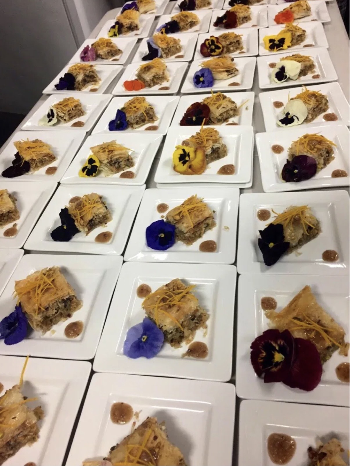Multiple plates with dessert slices, garnished with colorful edible flowers and toppings, arranged on a table.