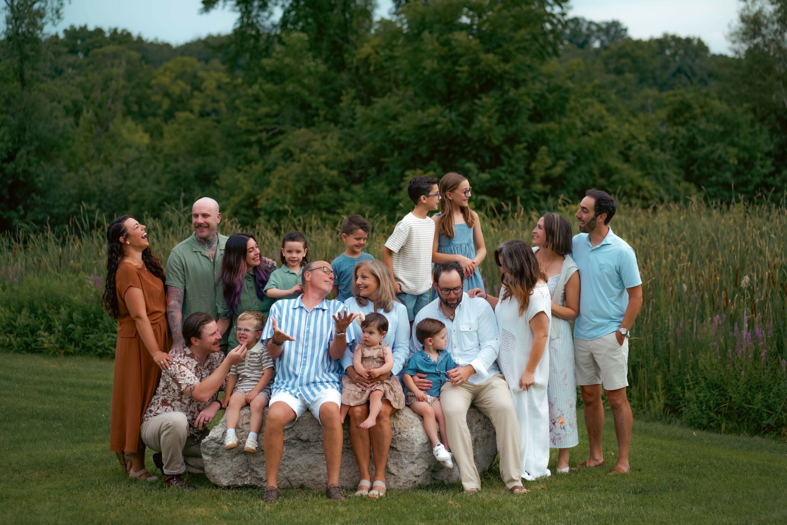 Group of people outdoors on grass with trees in background, some sitting and others standing, posing for photo.