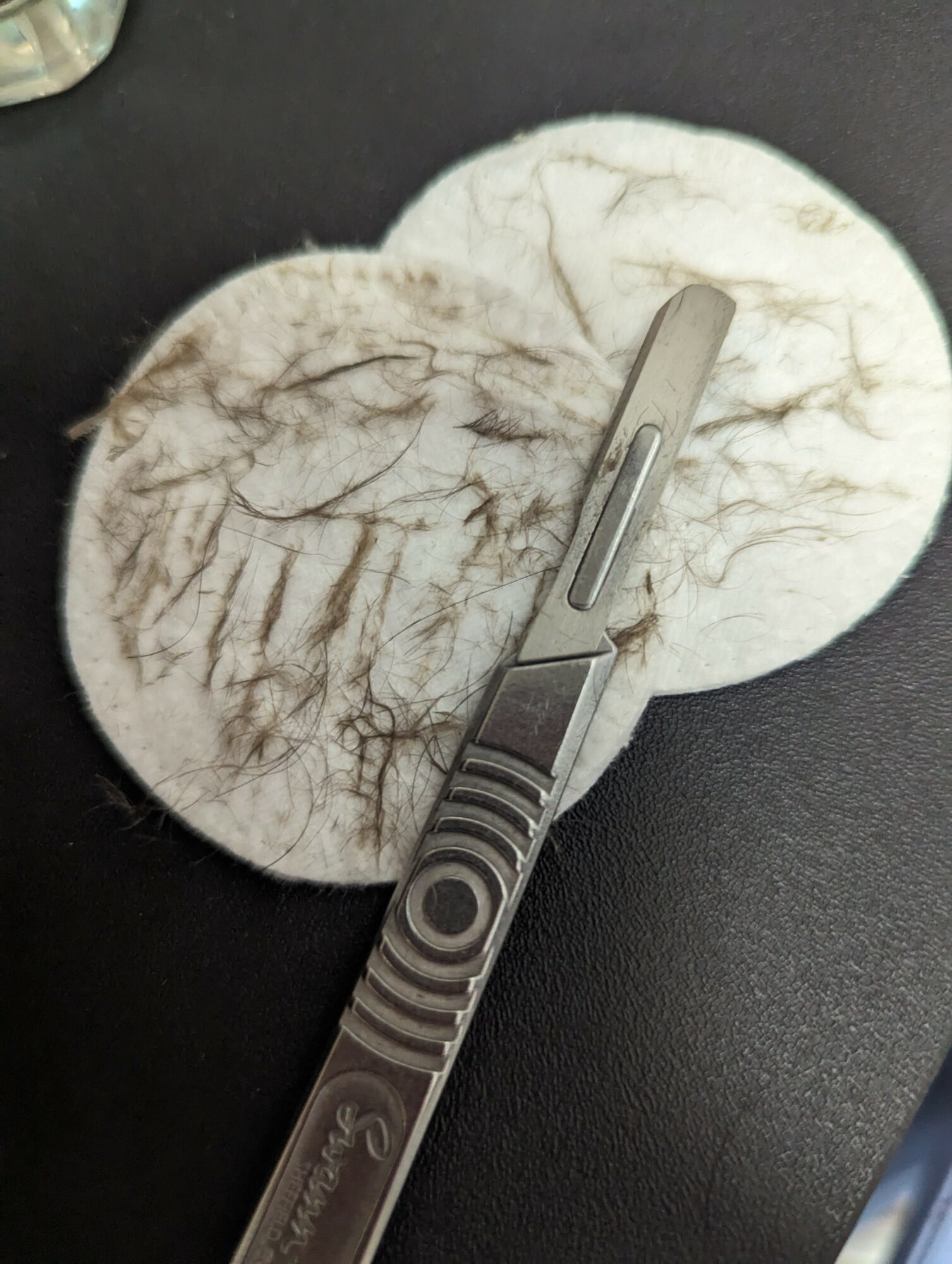 A metal tool resting on a round, textured surface with brown and white markings, on a dark background.