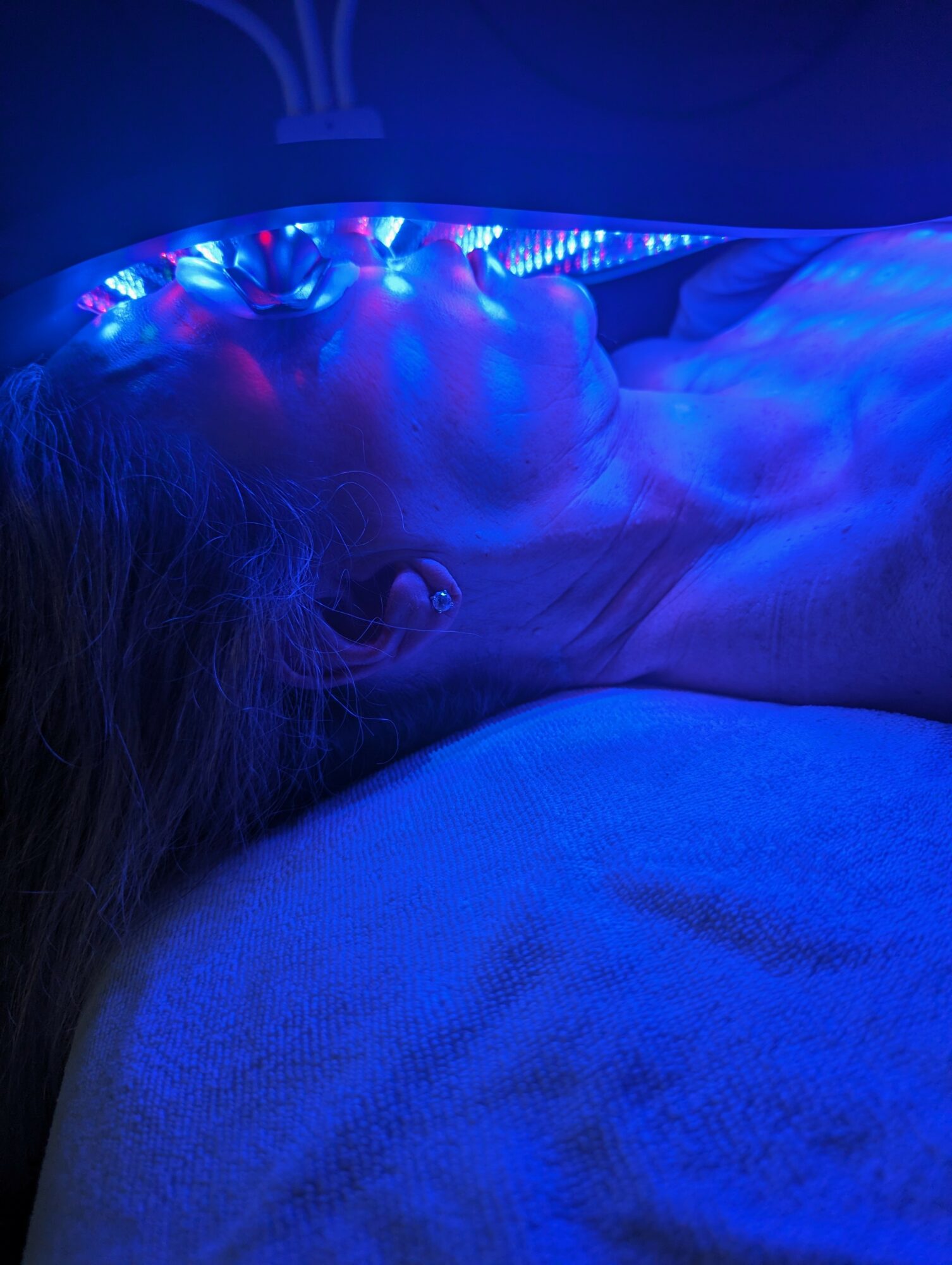 Person lying under blue LED lights, with head turned to the side, in a dark room.