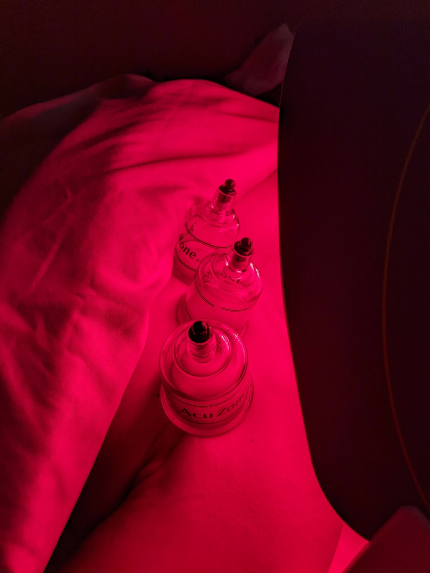 Person lying down with three small bottles on their thigh, illuminated by red light.