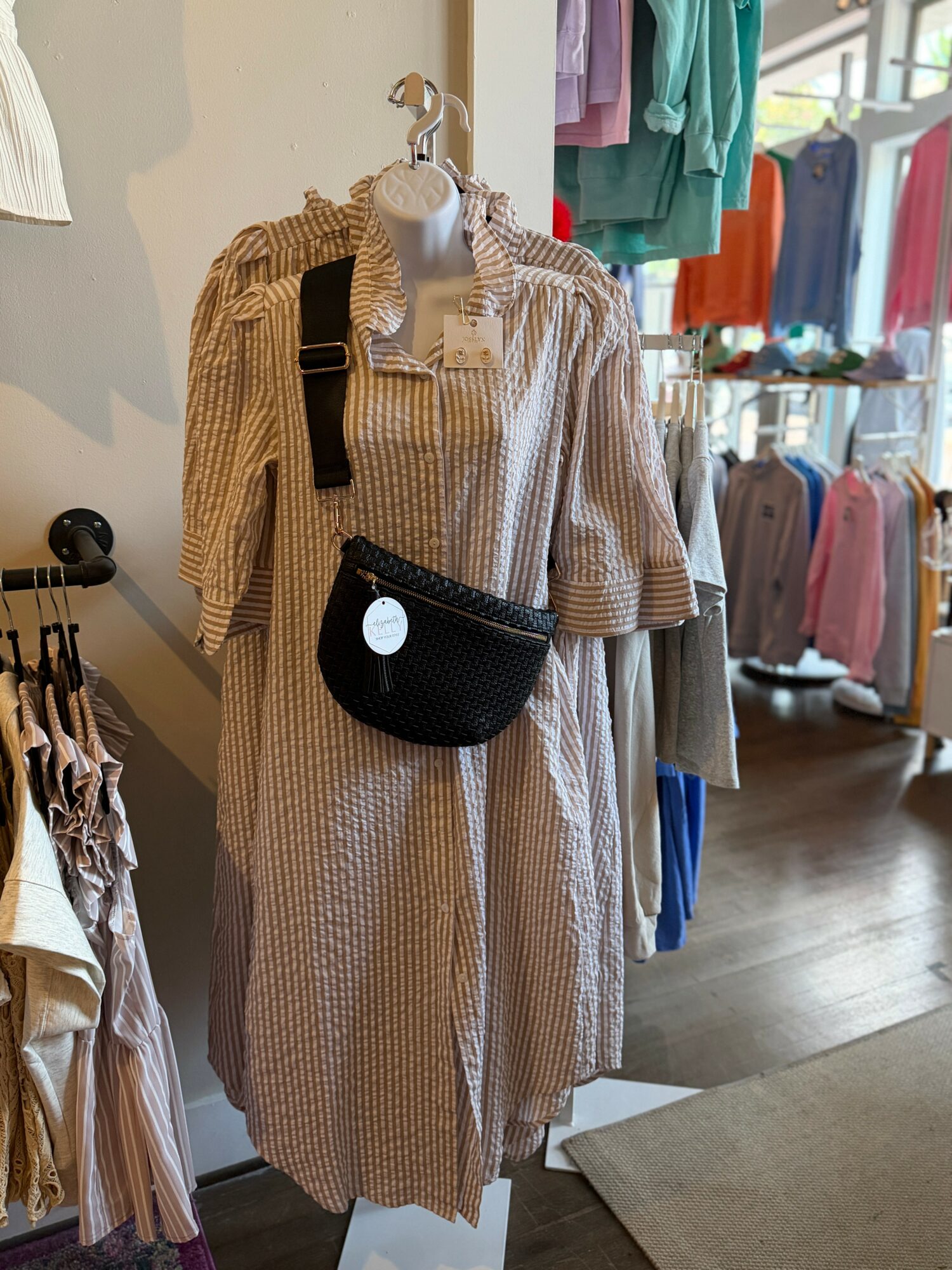 Mannequin dressed in a striped, long-sleeve shirt with a black crossbody bag, in a clothing store.