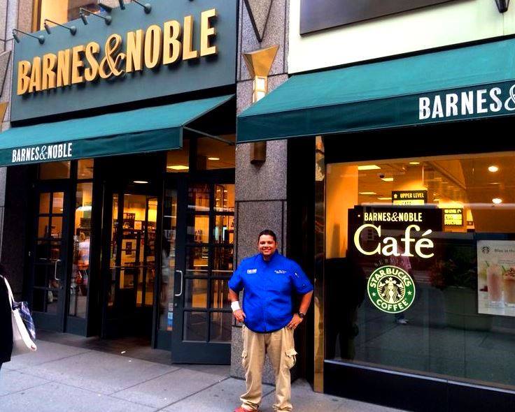 Barnes & Noble bookstore and Starbucks cafe storefront with a person standing outside, smiling, in front of the window.