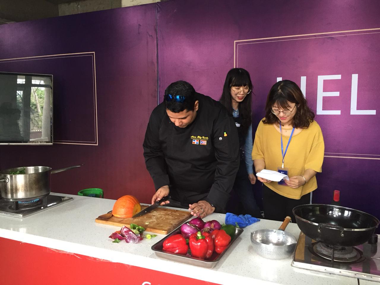 Three women in a kitchen with purple walls, preparing food on a white counter with apples and vegetables, smiling and talking.
