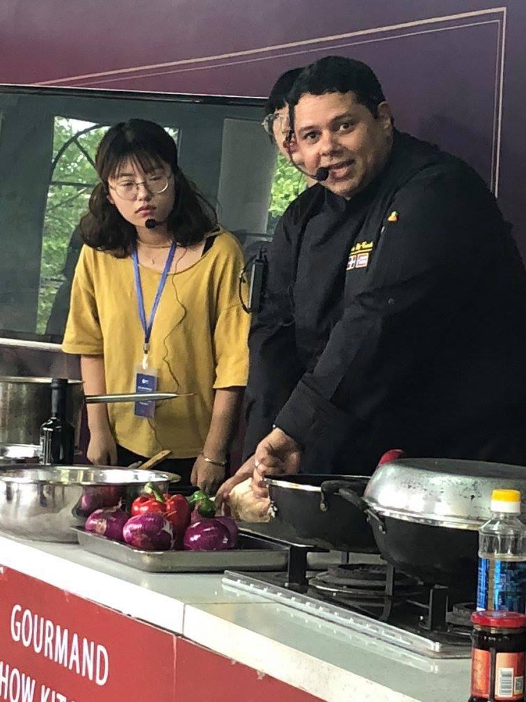 Two people, one in a black chef's uniform and the other in a yellow shirt, preparing food in a kitchen.