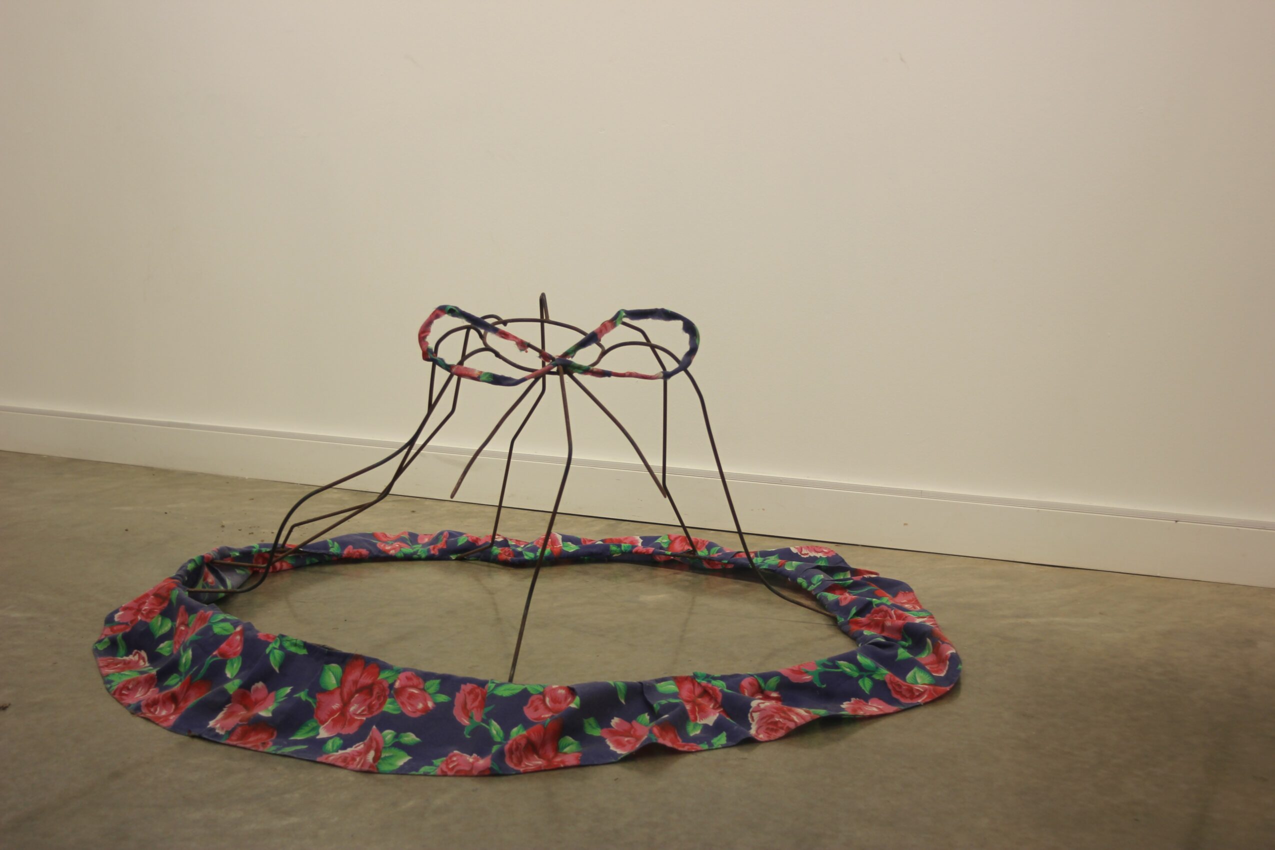A colorful fabric ring with wires and strings attached, placed on a floor against a plain wall.