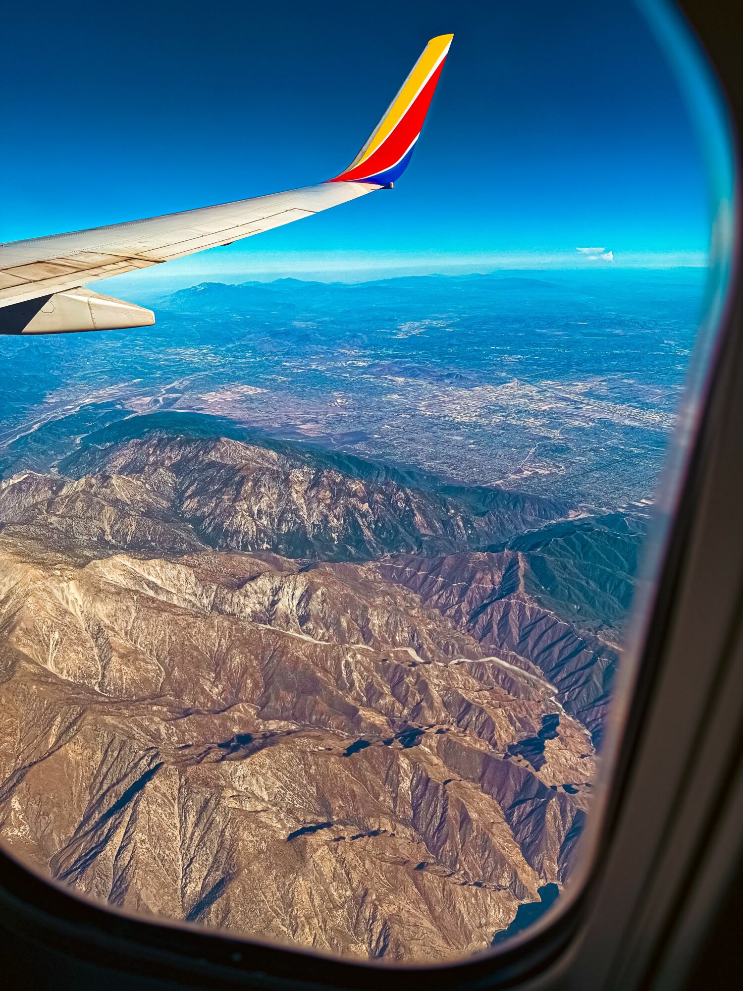 View from airplane window showing mountain landscape and part of wing with colorful tip.