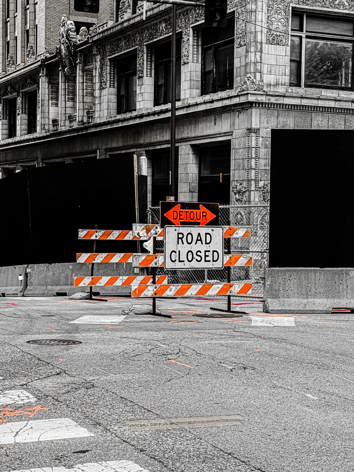 Street with road closed sign and detour arrow, construction barriers, and a building in the background.