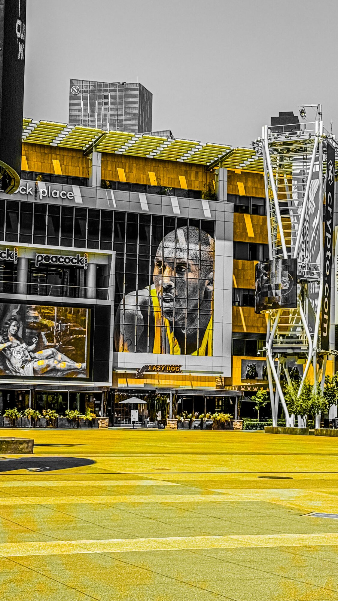 Cityscape with yellow and black building, large portrait mural, and Ferris wheel, with a yellow foreground and tall buildings in background.