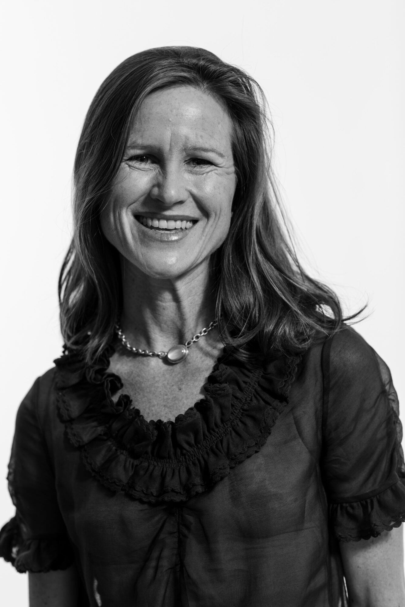 Smiling woman with shoulder-length hair wearing a ruffled blouse and necklace.