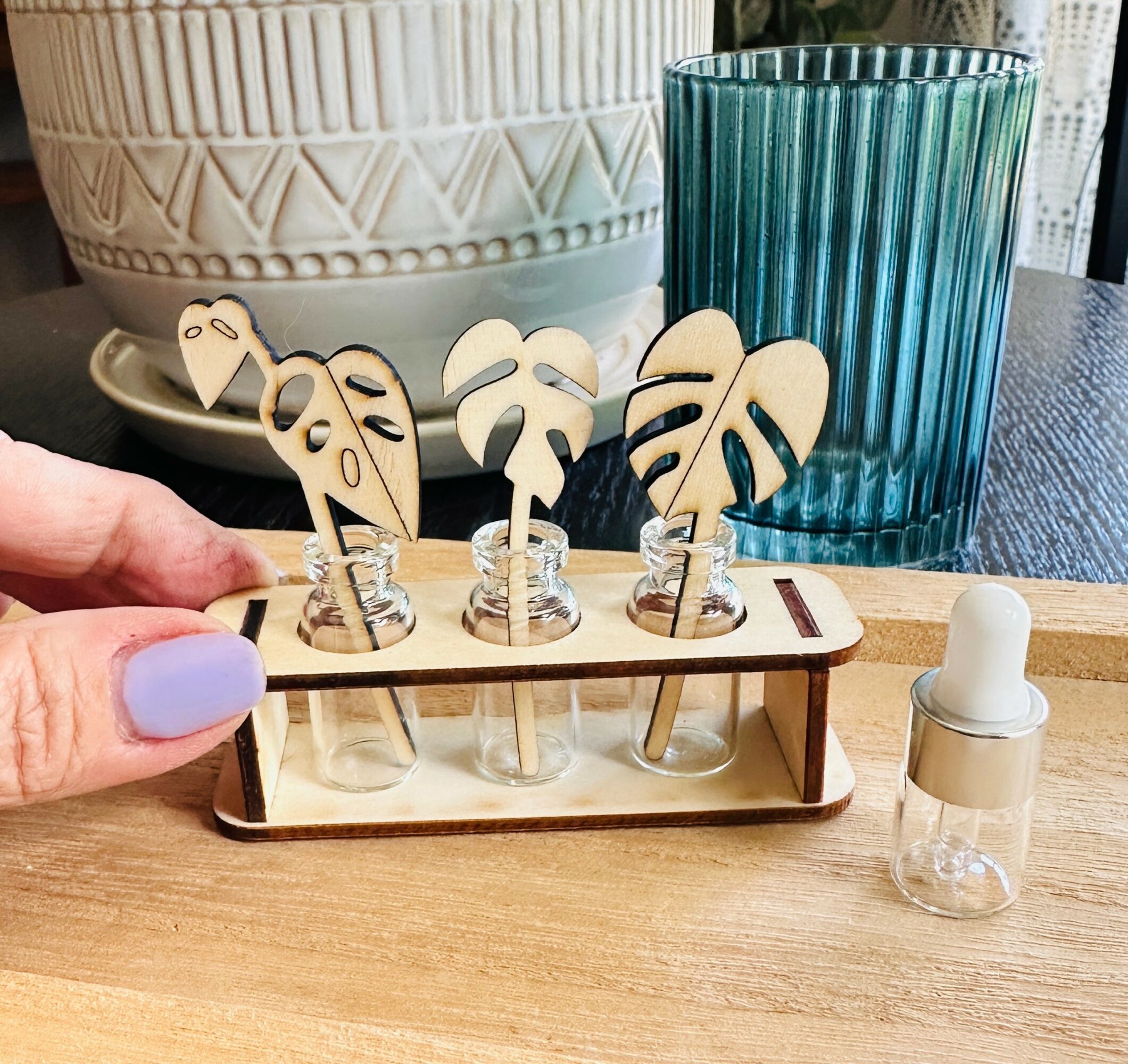 Wooden tray with four decorative plant-shaped cutouts, a small dropper bottle, and a large blue glass on a wooden table.