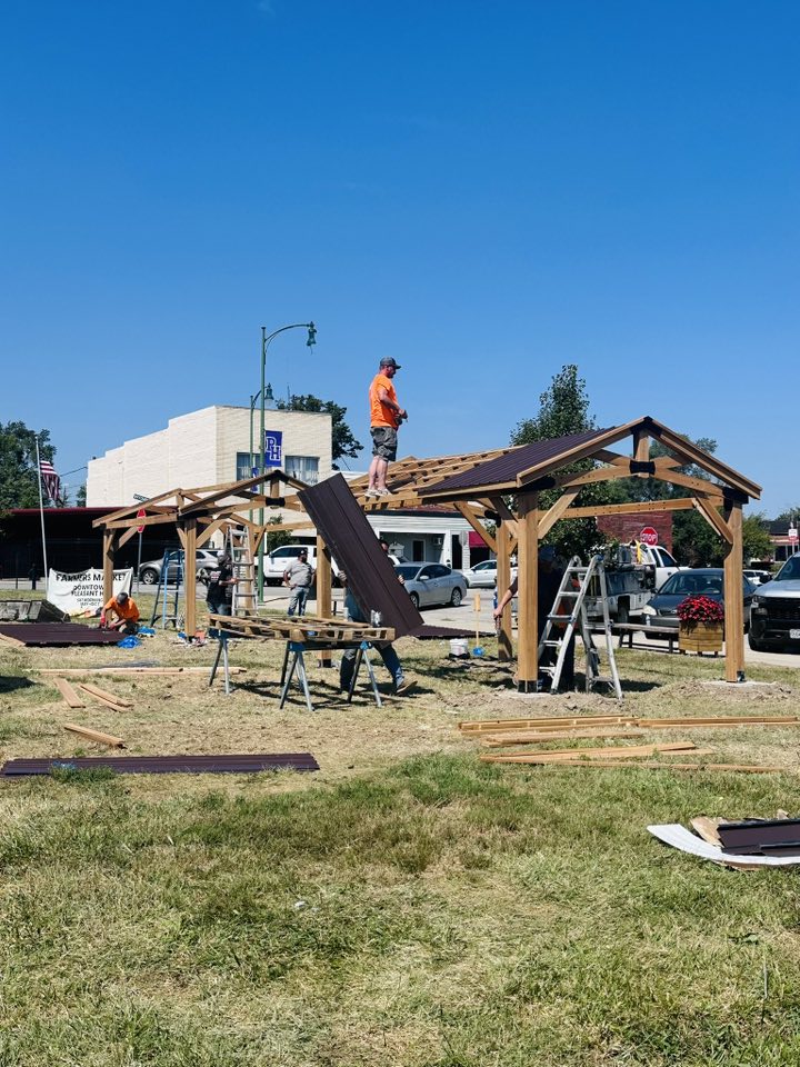 Person working on a construction site with wooden structures and tools, under a clear blue sky.