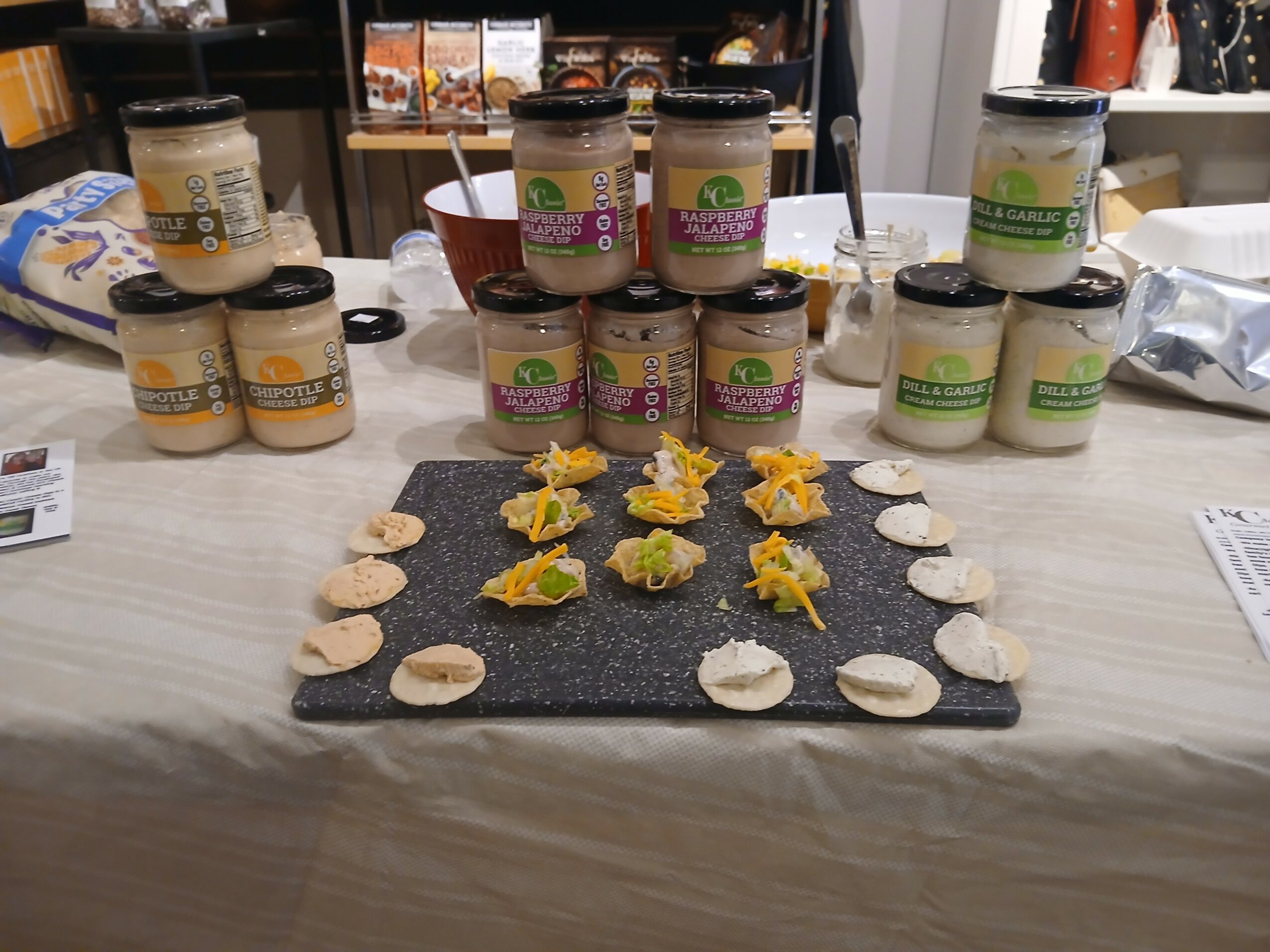Assorted jars of peanut butter and a snack platter with crackers and toppings on a table.