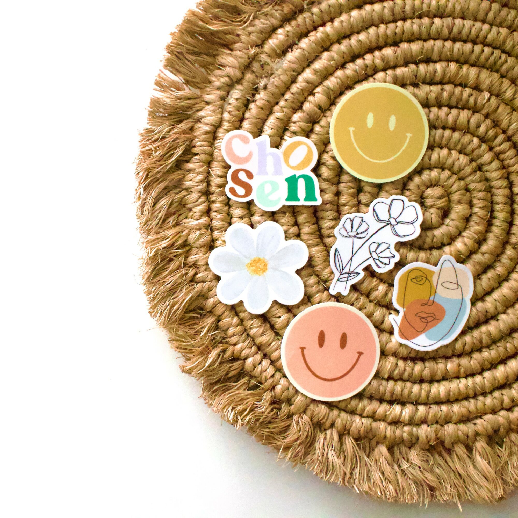 Decorative woven mat with smiley face stickers, a flower, a drawing, and colorful letters, on a white background.