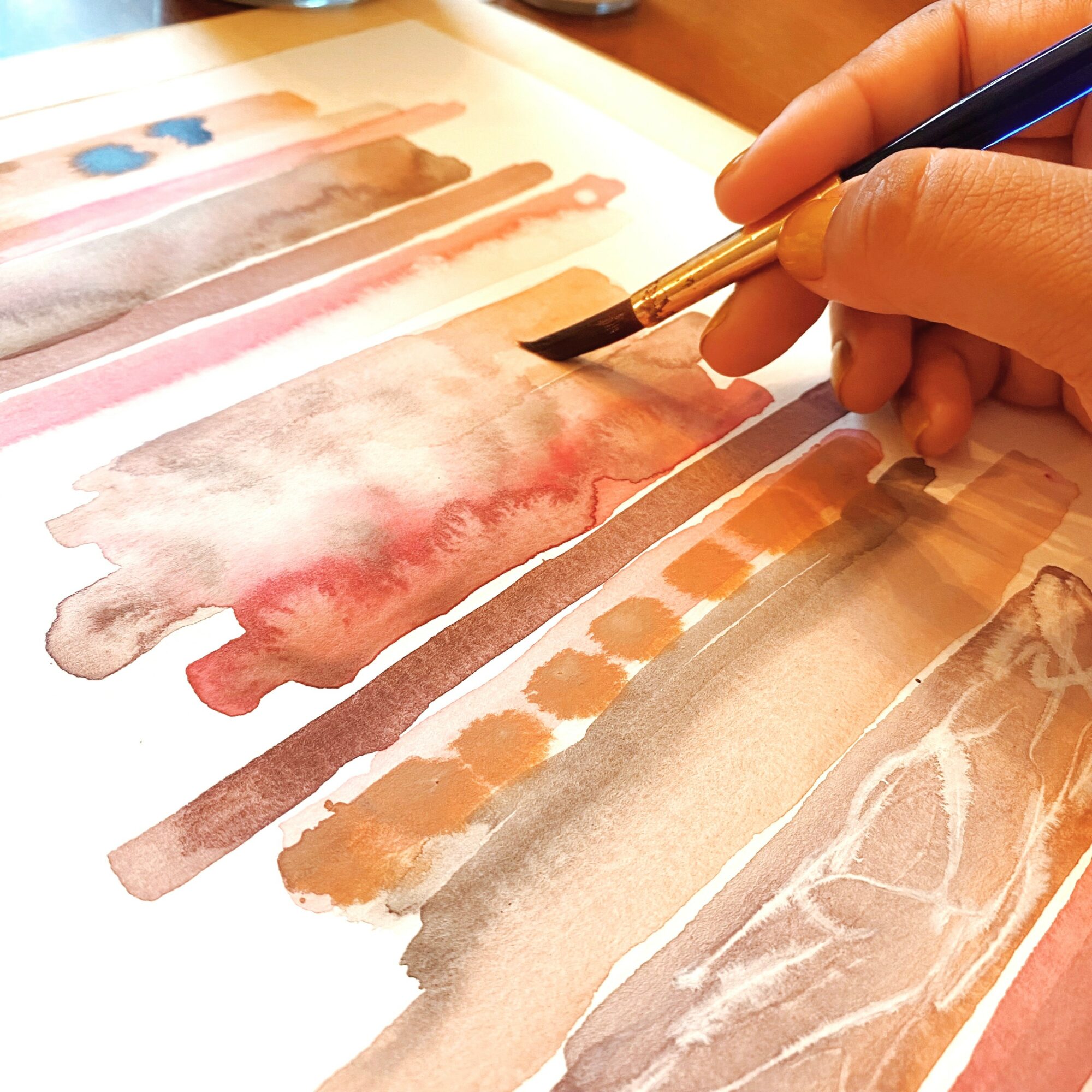 Close-up of a hand holding a paintbrush, creating watercolor art with various colors on paper.