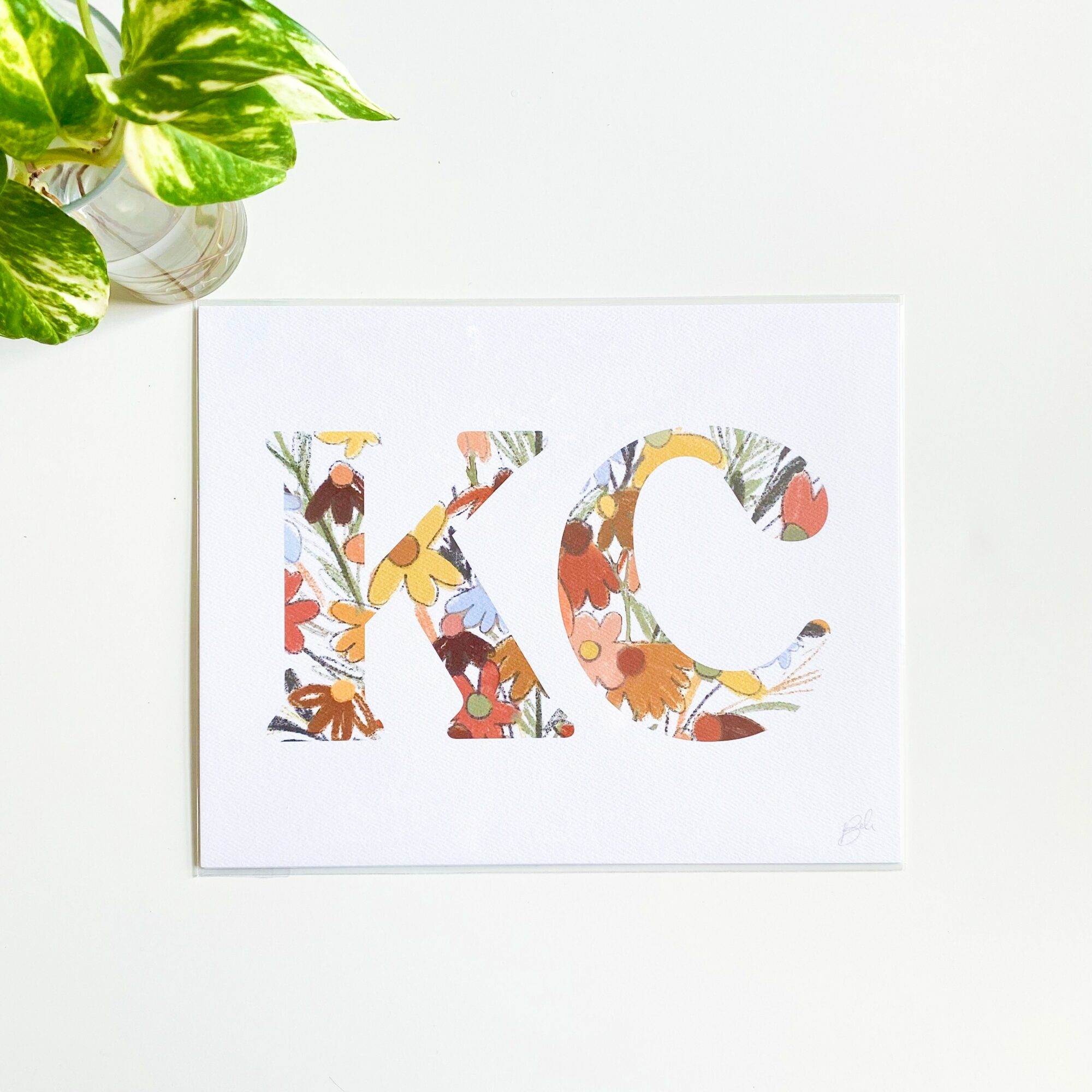 Letter 'XC' with floral and animal illustrations, on white background, in a frame, with green plant in top left corner.
