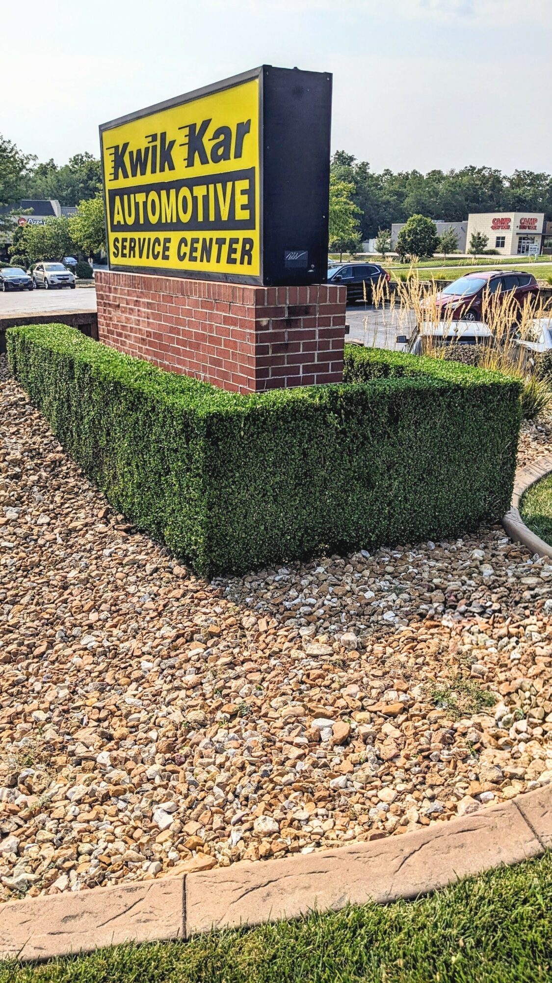 Kwik Kar Automotive Service Center sign on brick base with trimmed hedge and gravel foreground.