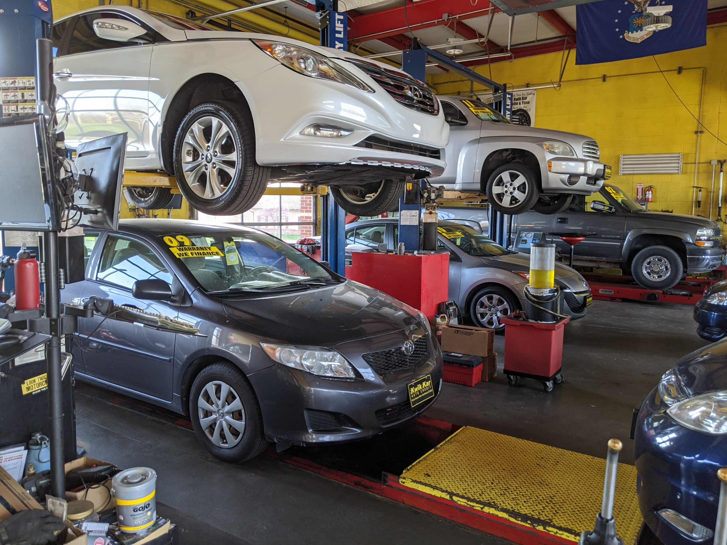 Car inside a garage with a vehicle lift and other cars, tools, and equipment visible in the background.