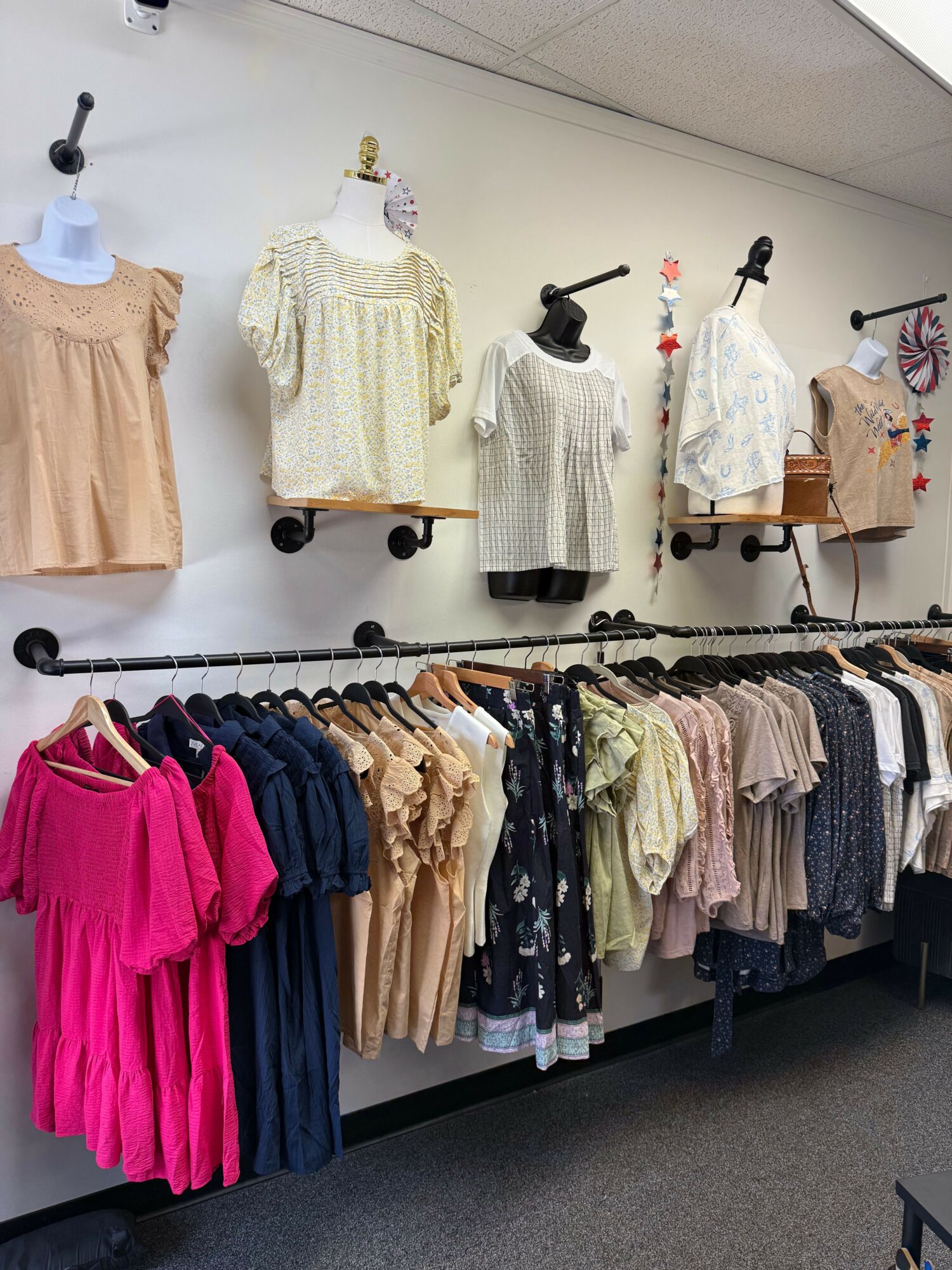 Clothing display with mannequins dressed in sweaters and dresses, and racks of folded and hanging clothes in a store.