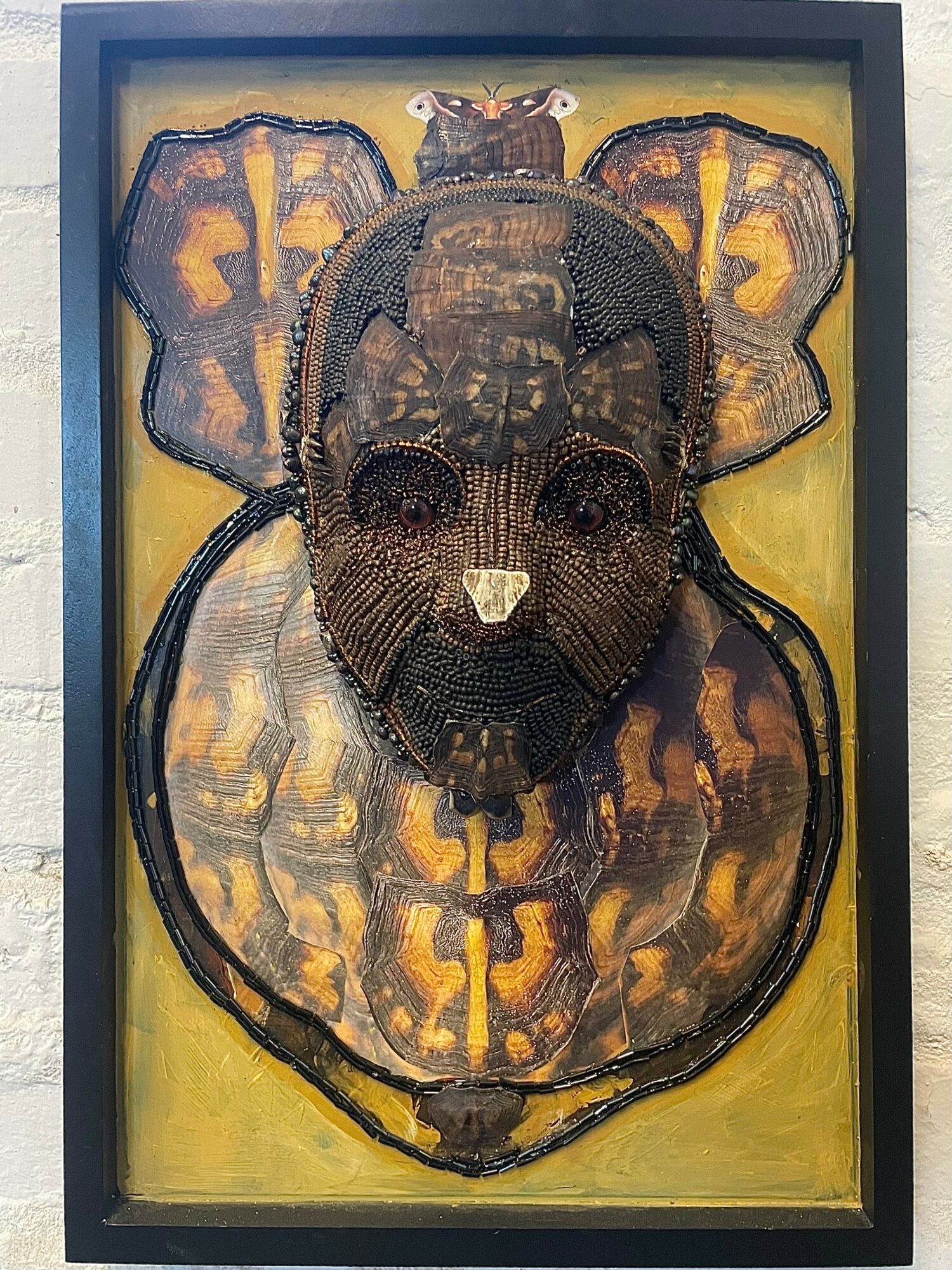 Framed artwork of a bear's face with butterfly wings on a yellow background.